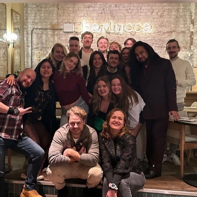 Group of people smiling and posing for a photo in a restaurant with a sign that says 'Handmade' in the background.
