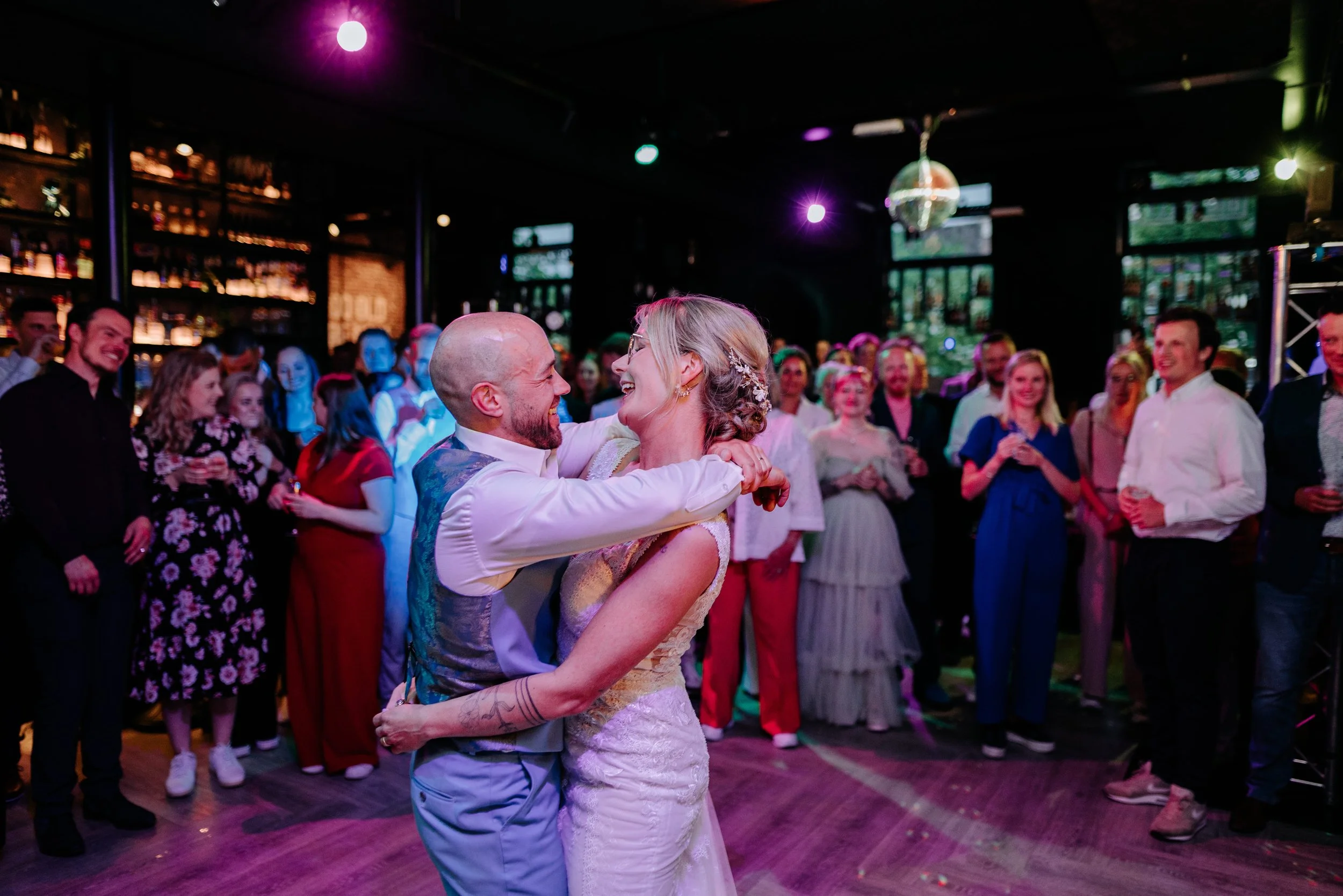A bride and groom are dancing closely at their wedding reception, surrounded by guests watching happily.