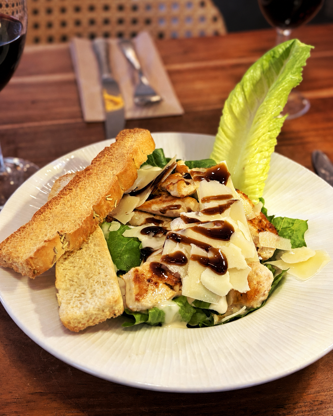 Chicken Caesar salad with Parmesan cheese shavings, croutons, and a romaine lettuce leaf on a white plate