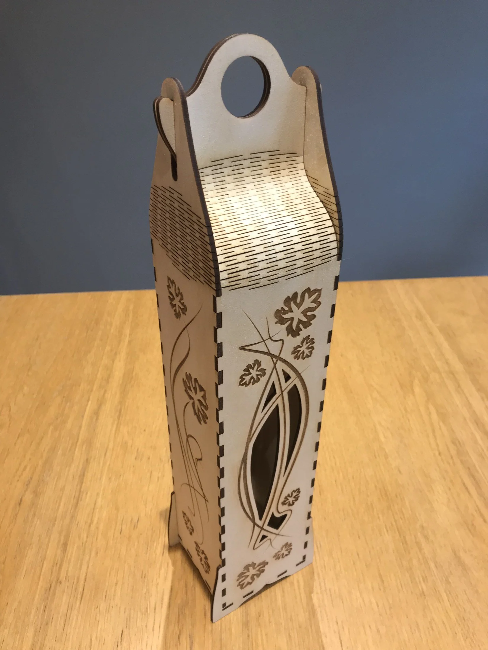 Wooden gift carrier with a slotted flexible shoulder and decorative cut-outs.