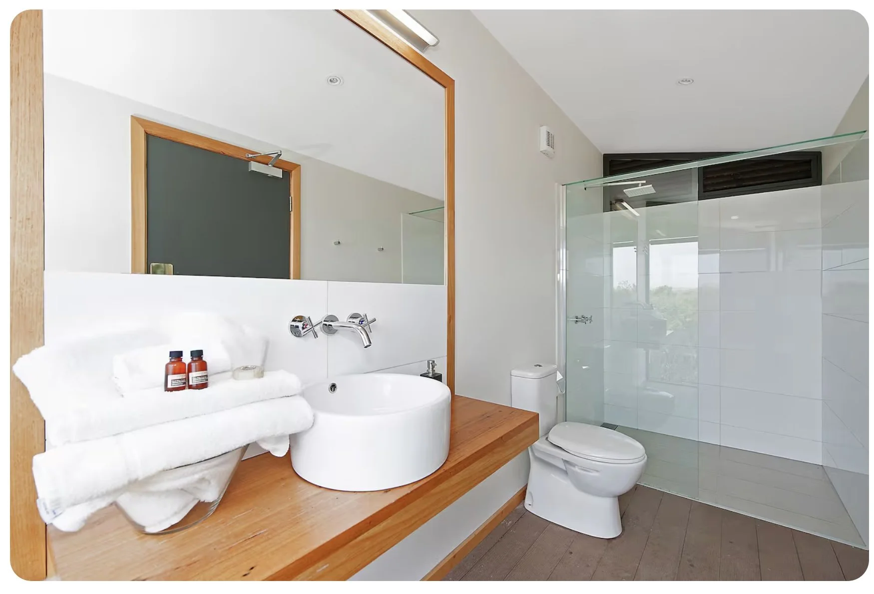 Modern bathroom with a white sink, mirror, towel, toiletries, and a glass-enclosed shower area.