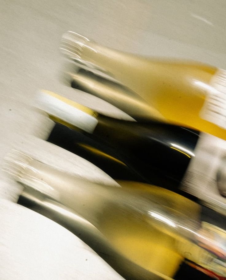 Blurred image of a pile of various bottles, including wine, liquor, or champagne bottles on a gray surface.