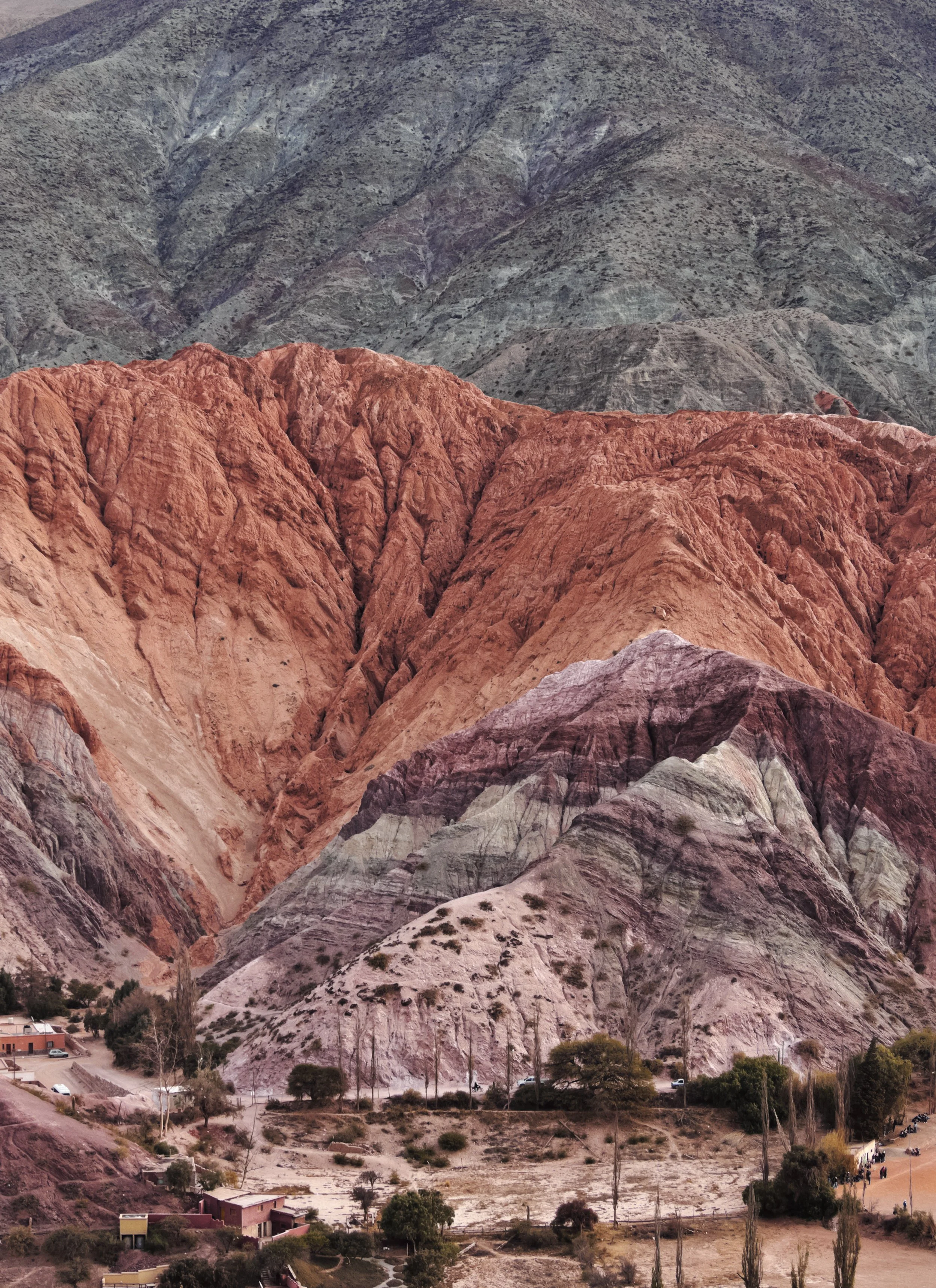 Montañas rosadas y grises con vegetación escasa, casas pequeñas en la base y árboles dispersos en un paisaje árido.
