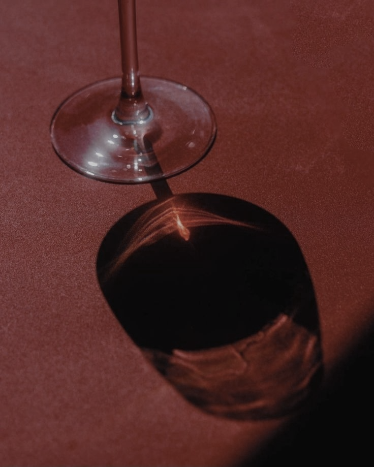 A glass of red wine with a reflection of the glass's shadow on a reddish surface