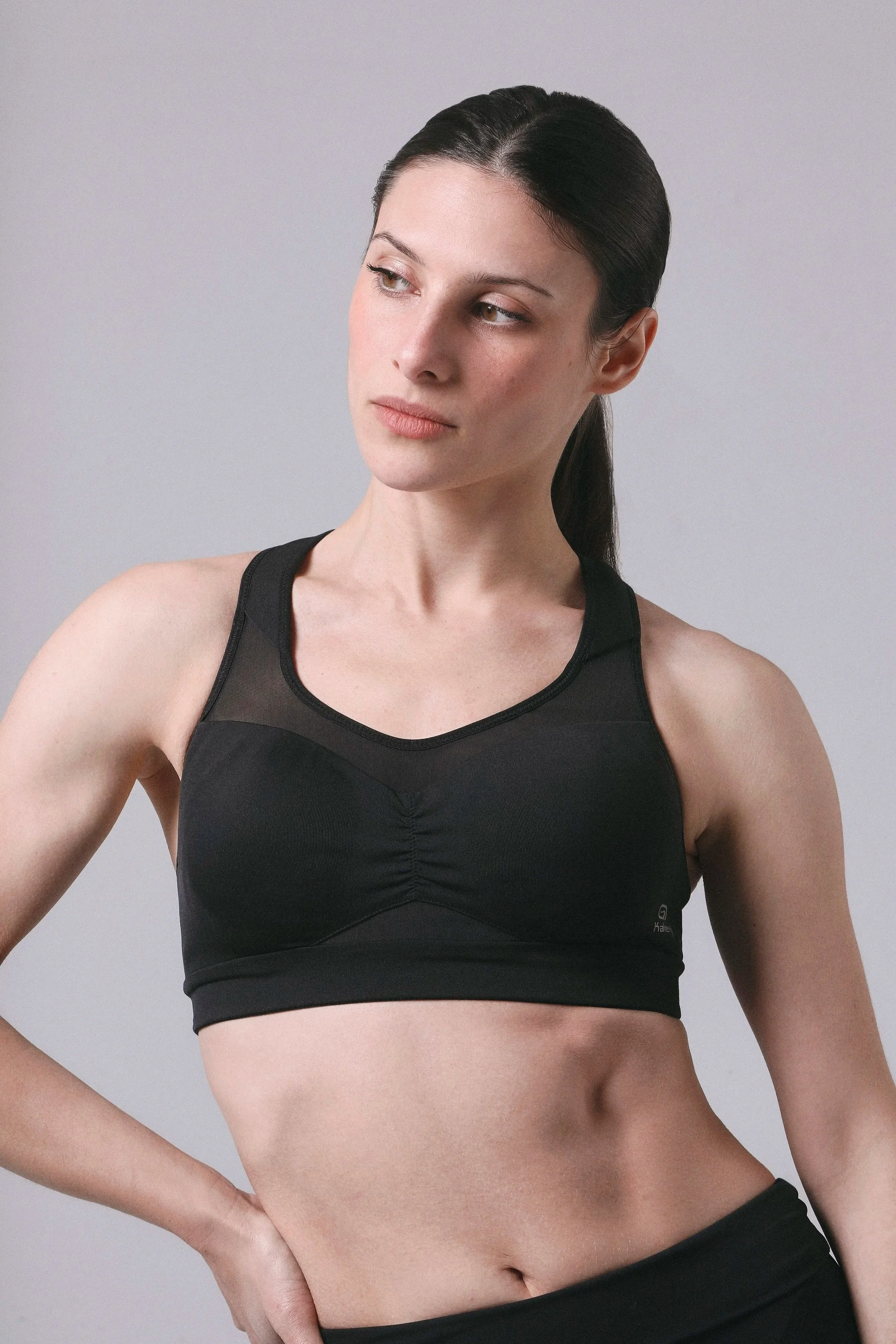 Mujer con cabello oscuro atado, vestida con top negro deportivo, mostrando su abdomen.