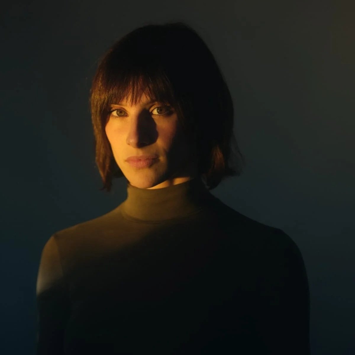 Nina Pomodoro, French-Spanish actress, headshot, Barcelona Retrato de una mujer con cabello corto y oscuro, con iluminación suave que crea un contraste entre las áreas iluminadas y las sombras, en un fondo oscuro.
