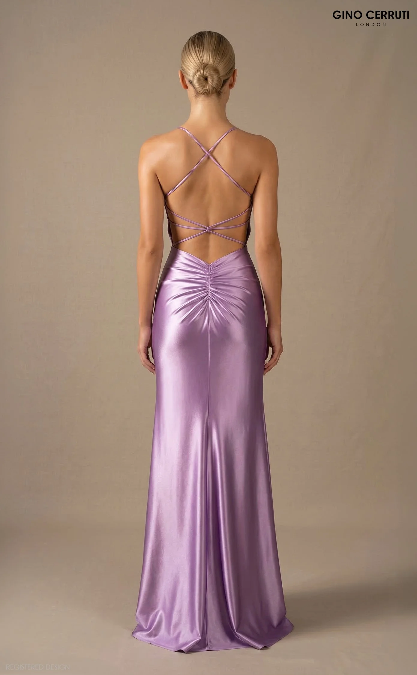 Back view of a woman wearing a lavender satin evening gown with a fitted bodice, ruched skirt, and delicate crisscross straps on the back.
