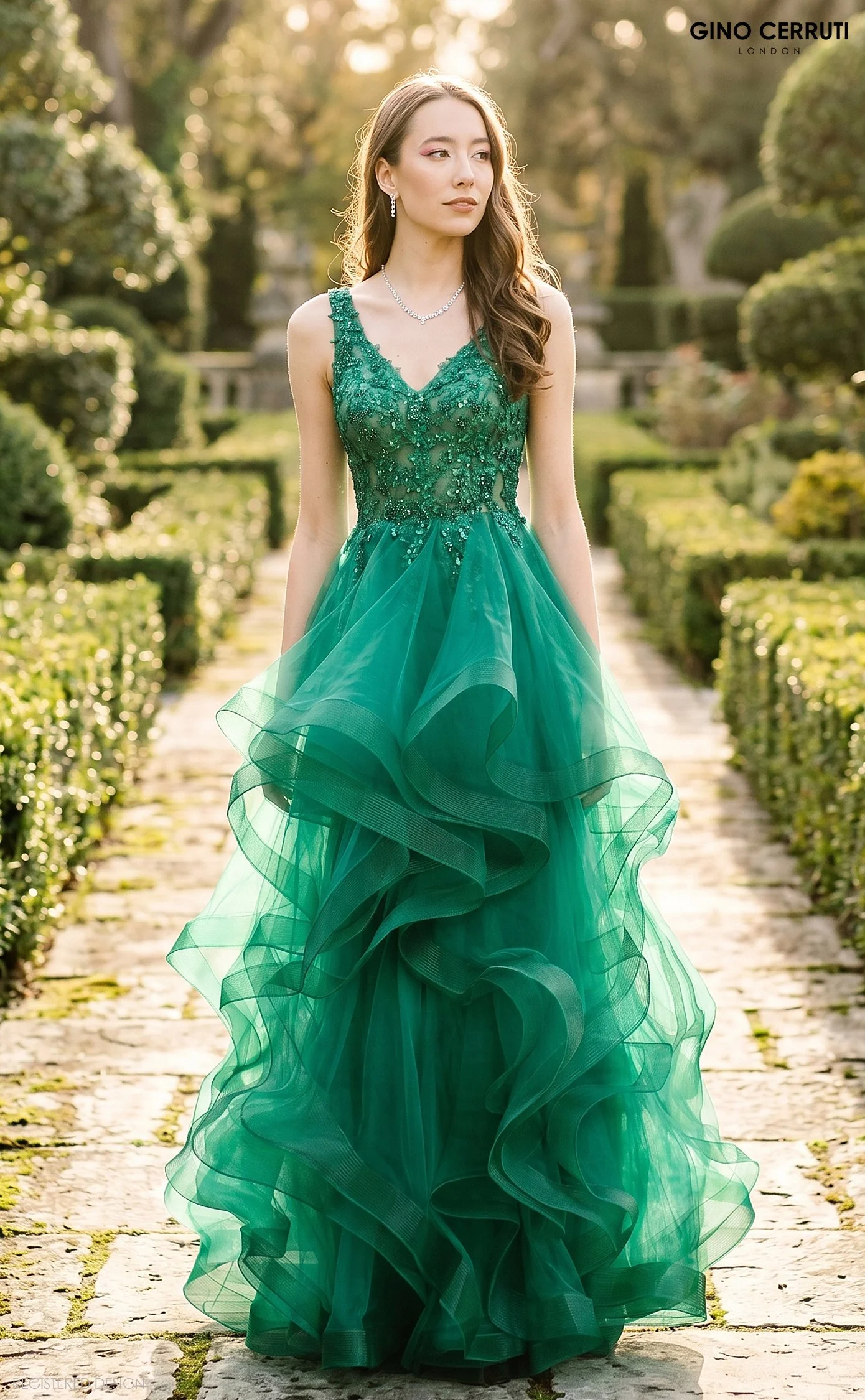 A woman wearing a flowing green dress with intricate beadwork, standing in a garden with sunlight filtering through trees.
