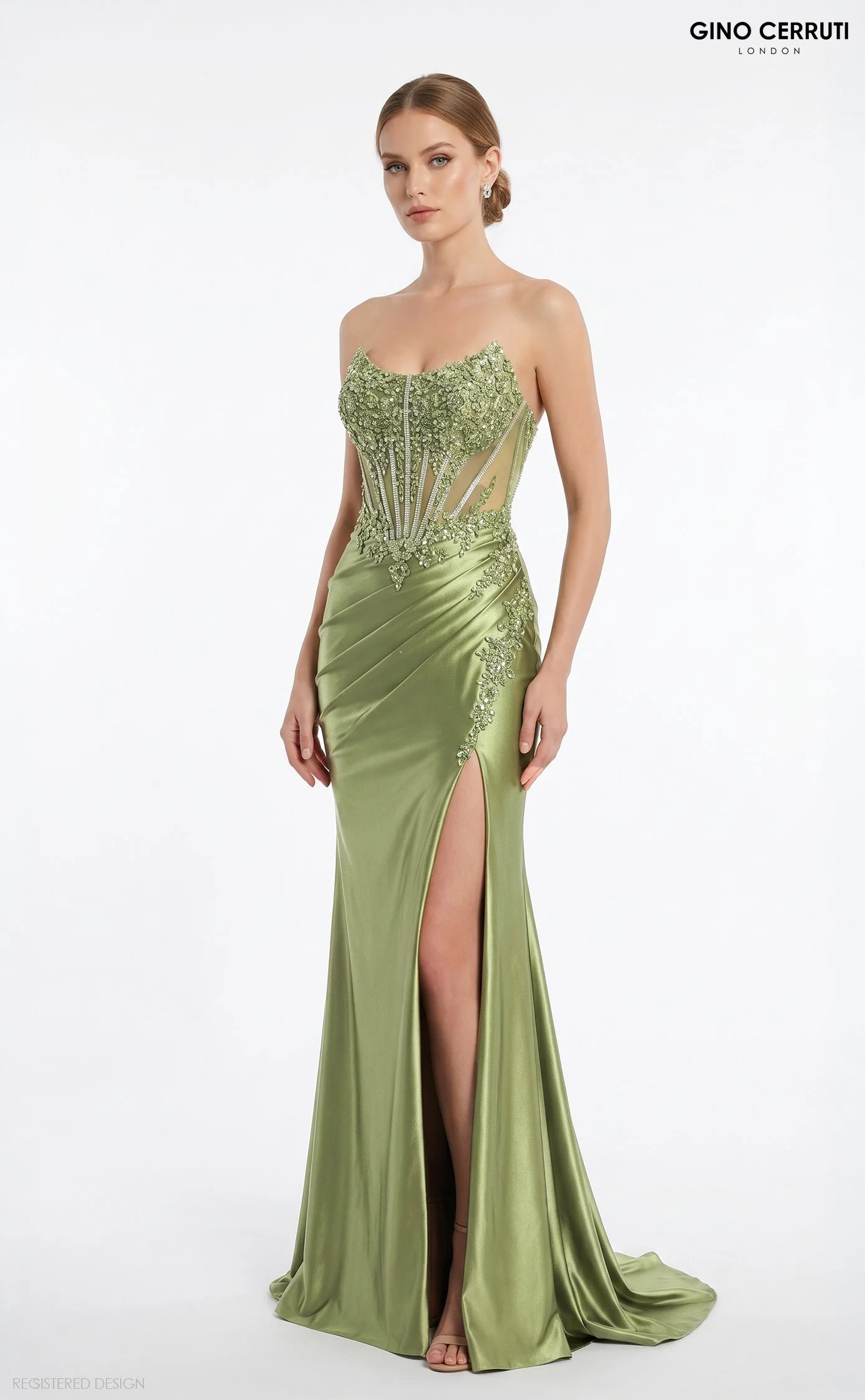 A woman in an elegant green evening gown with intricate beadwork and embroidery, featuring a thigh-high slit, standing against a plain white background.