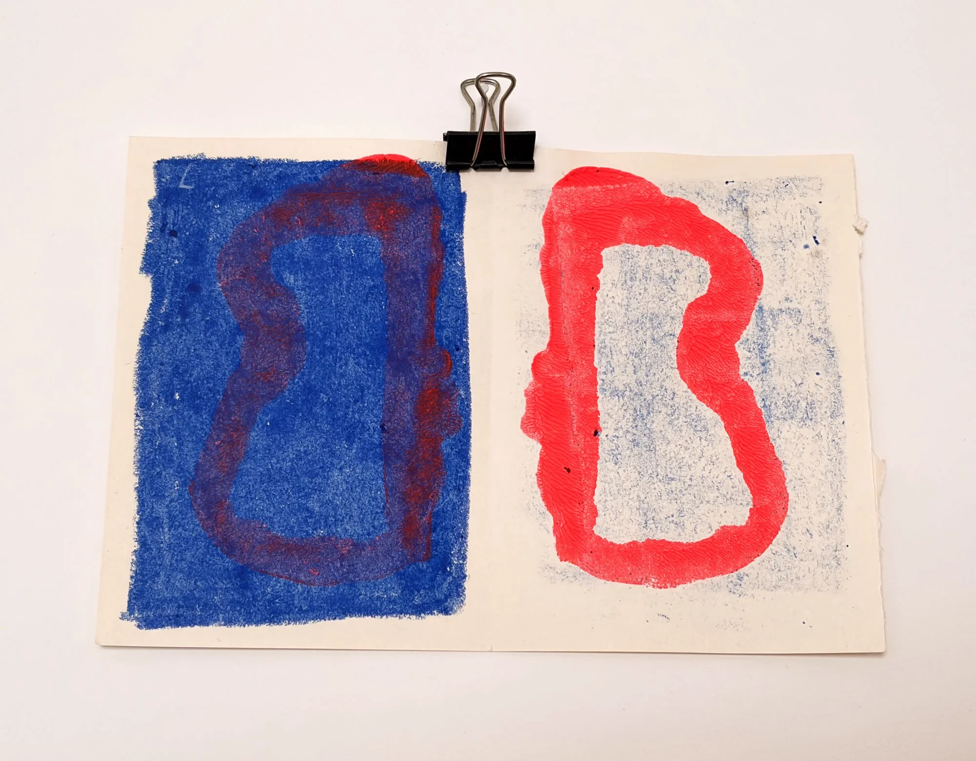 Dos hojas de papel con letras 'O' y 'L' en colores azul y rojo, sujetas con unclip negro.