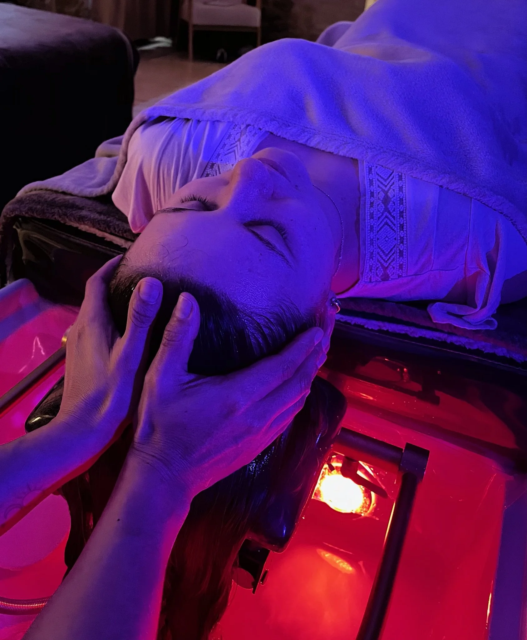 Personne allongée sur une table de soin Head Spa professionnelle, éclairée par une lumière douce. La personne a les yeux fermés et un visage détendu, elle profite d'une séance Head Spa de qualité qui lui apporte une profonde relaxation.