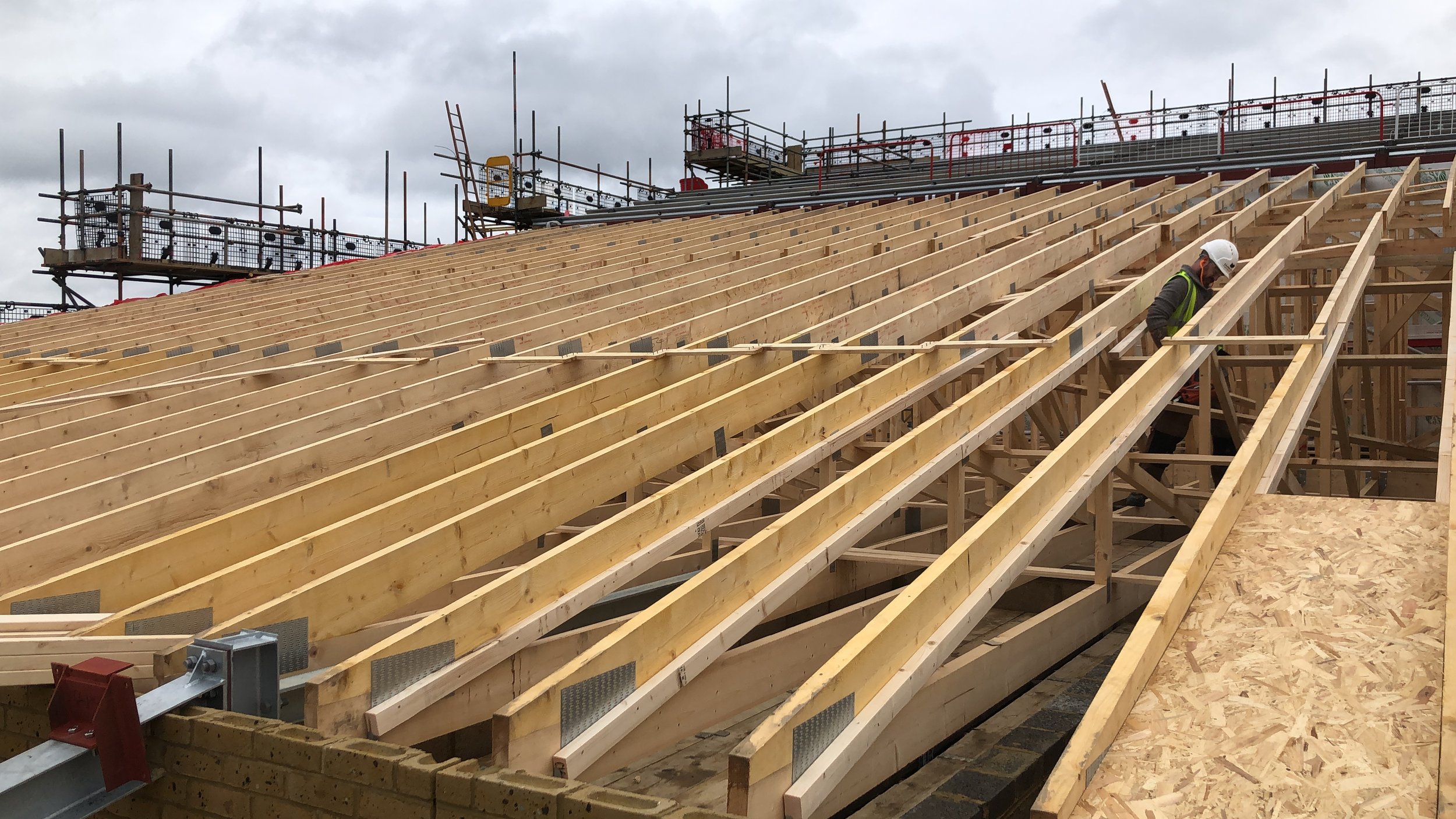Construction worker in safety gear installing wooden roof beams on a building under construction.