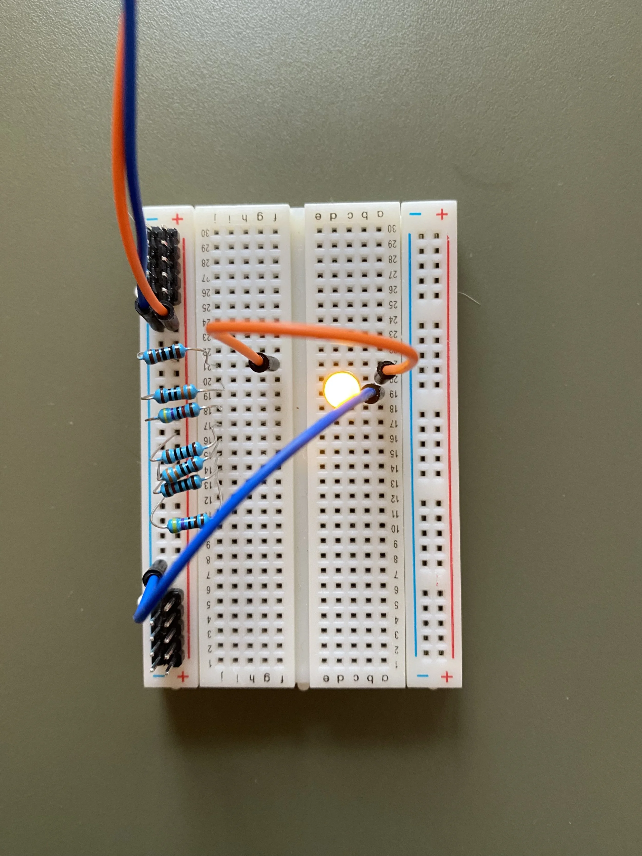 Breadboard with LED and wires testing different resistors on a green surface