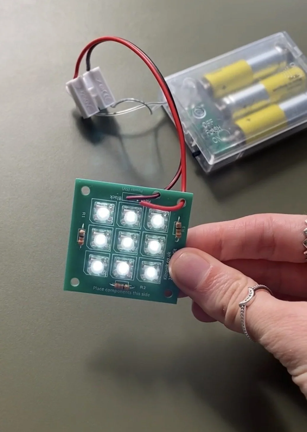 Square LED lit up and held by hand on green surface