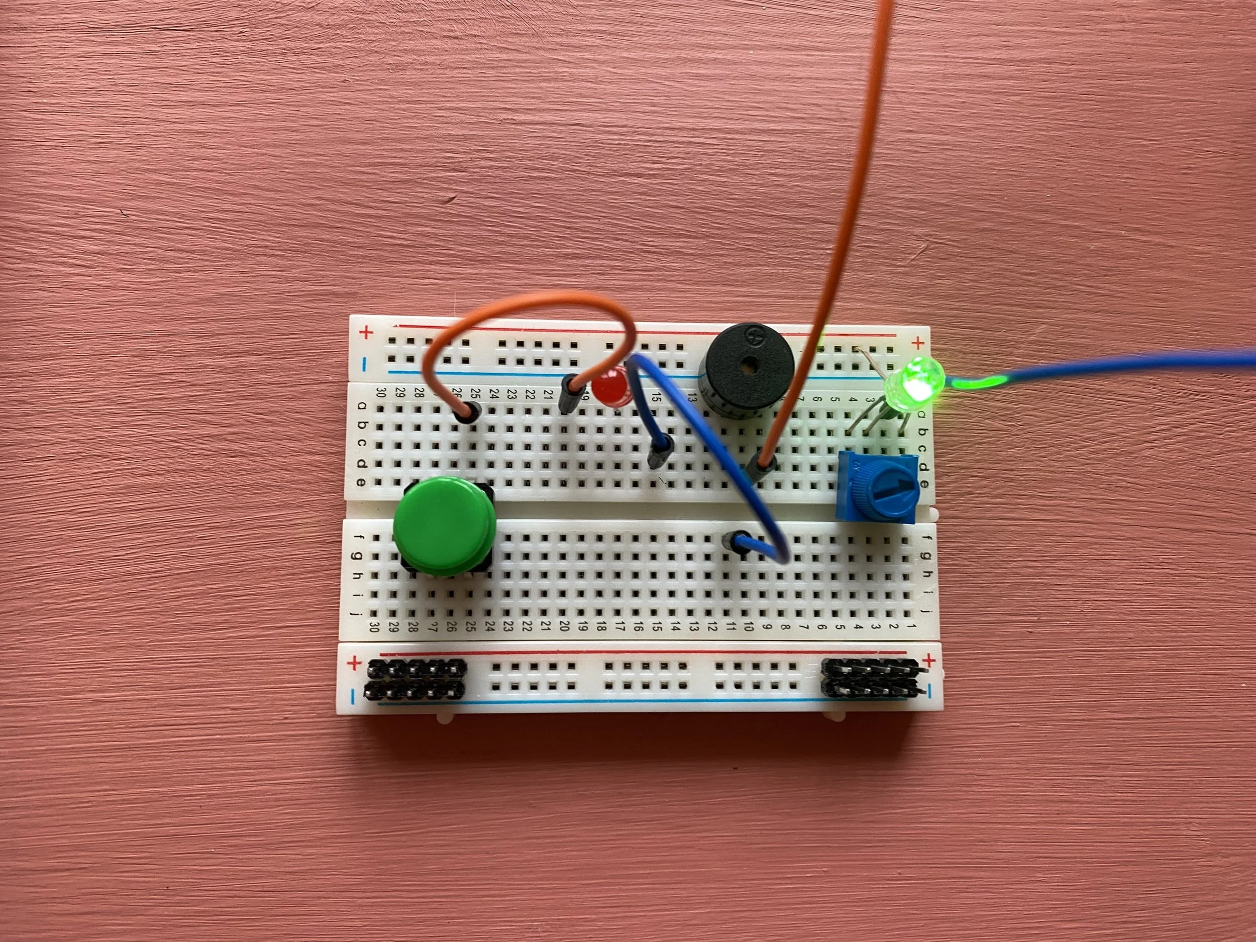 Advanced breadboard project with switch, LED, buzzer and wires on pink background