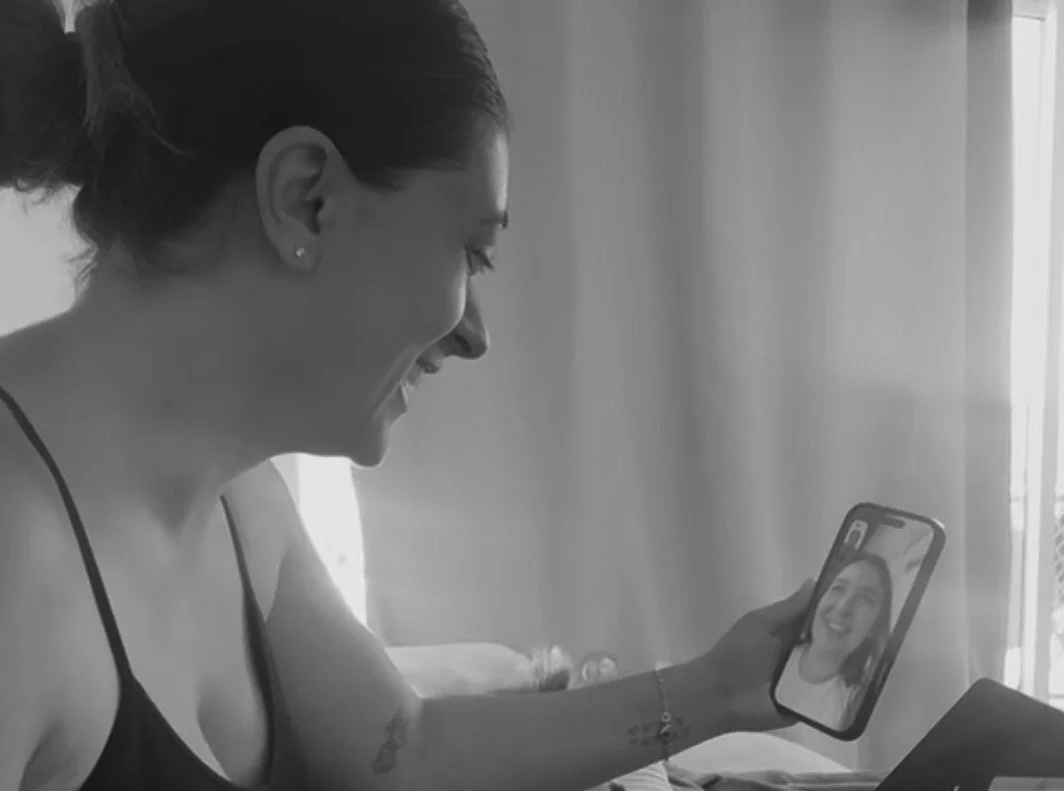 Une femme souriante regarde une vidéo sur son téléphone portable dans une pièce lumineuse.