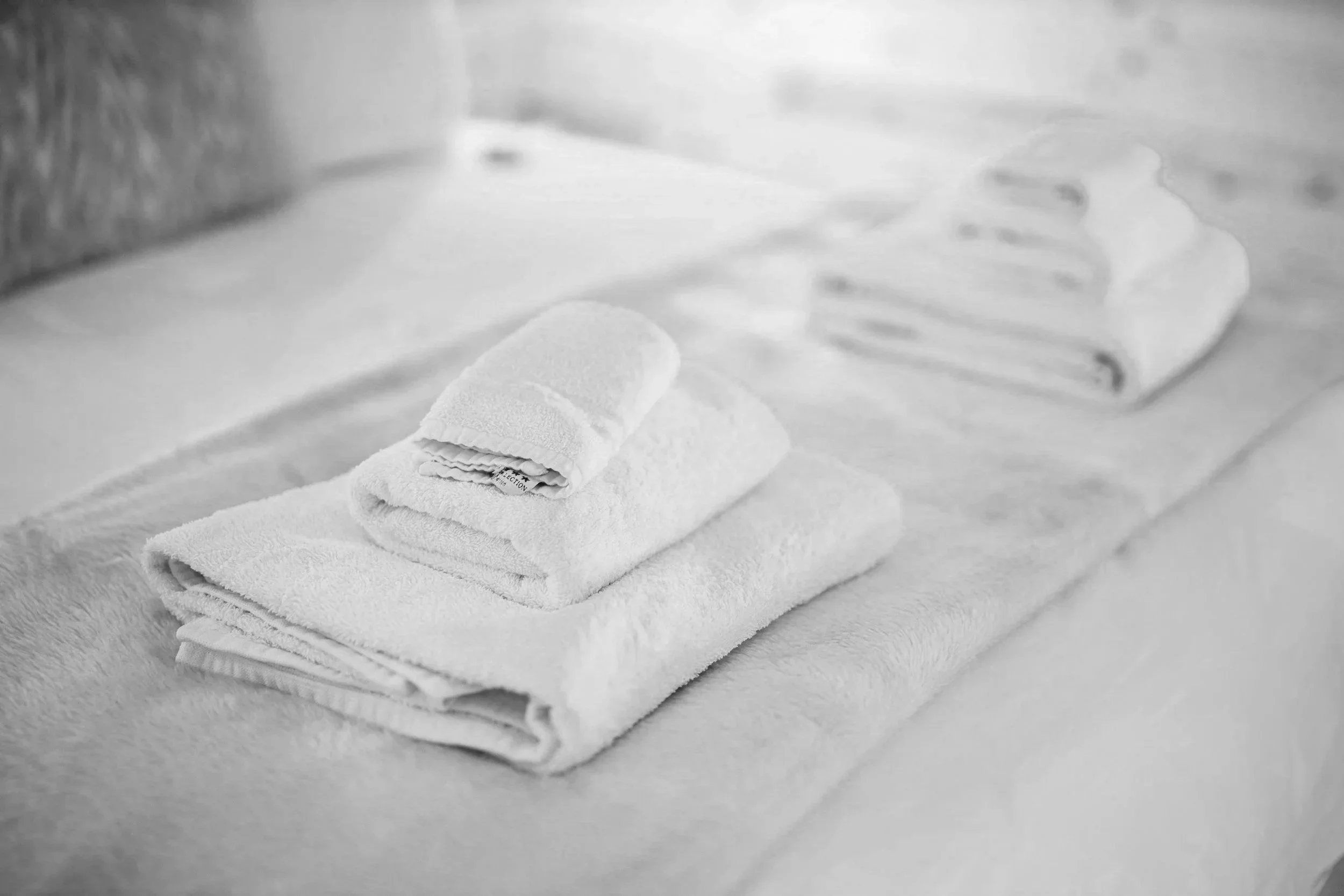 White towels neatly folded on a soft surface with a small rolled towel on top.