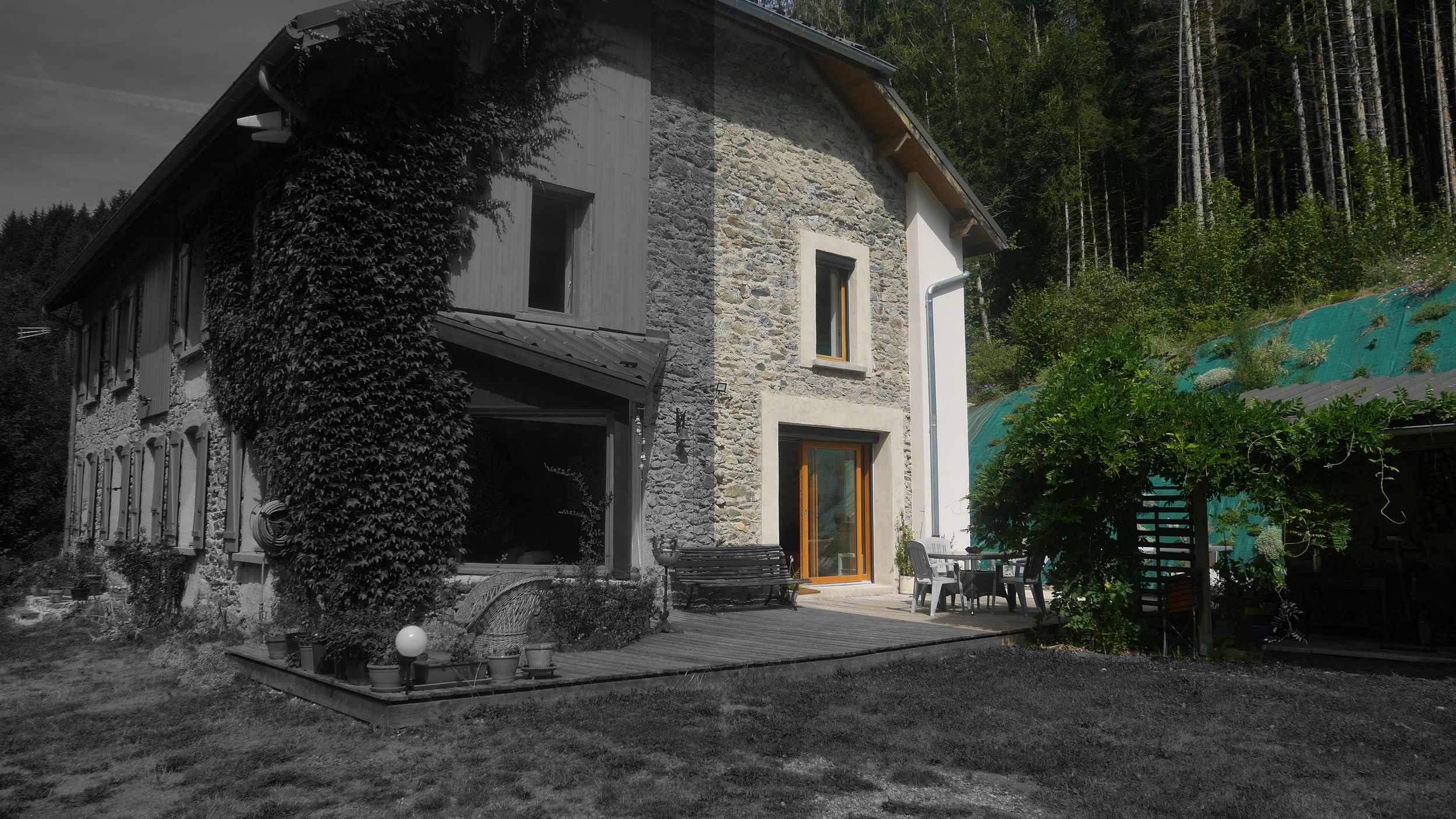 A house with a stone facade, surrounded by greenery and trees, with a patio area featuring outdoor furniture and potted plants.