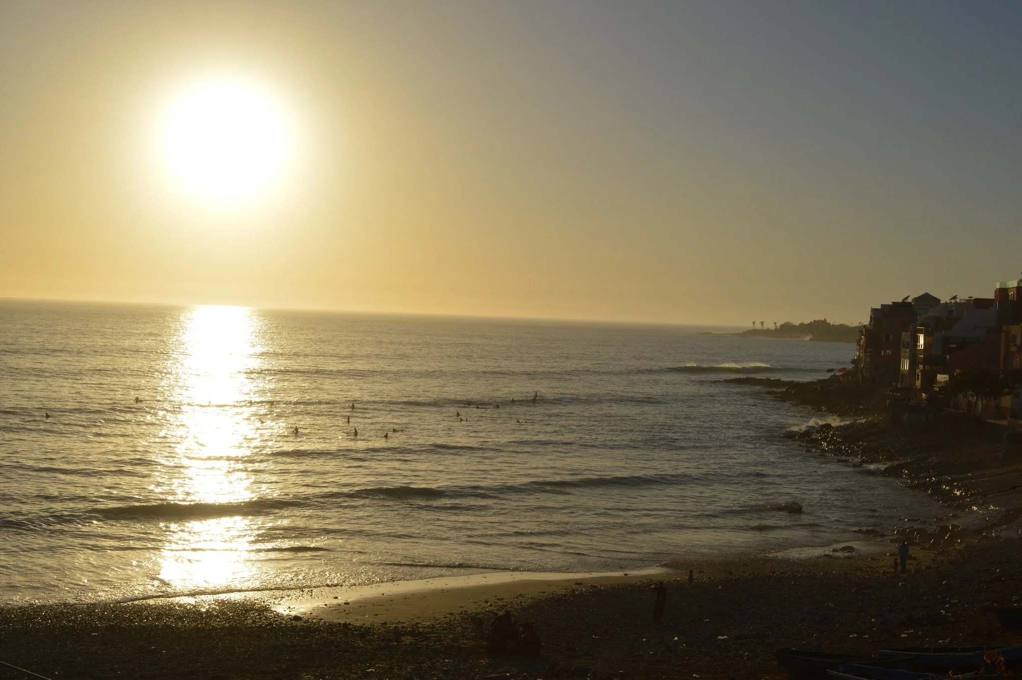Sunset over the ocean, with waves and beachfront buildings on the right.
