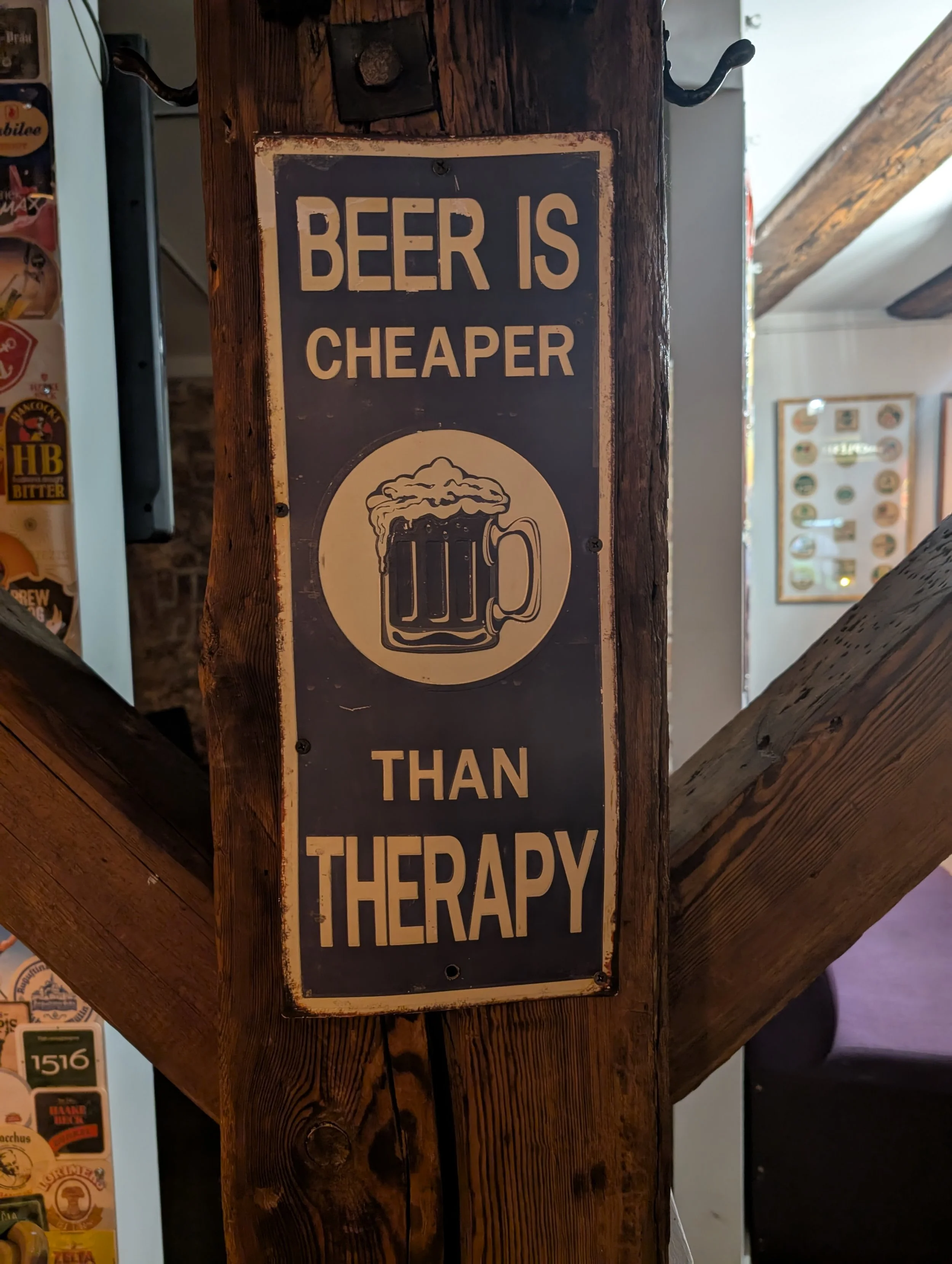 A vintage metal sign on a wooden post that reads, 'Beer is Cheaper Than Therapy,' featuring a graphic of a beer mug.