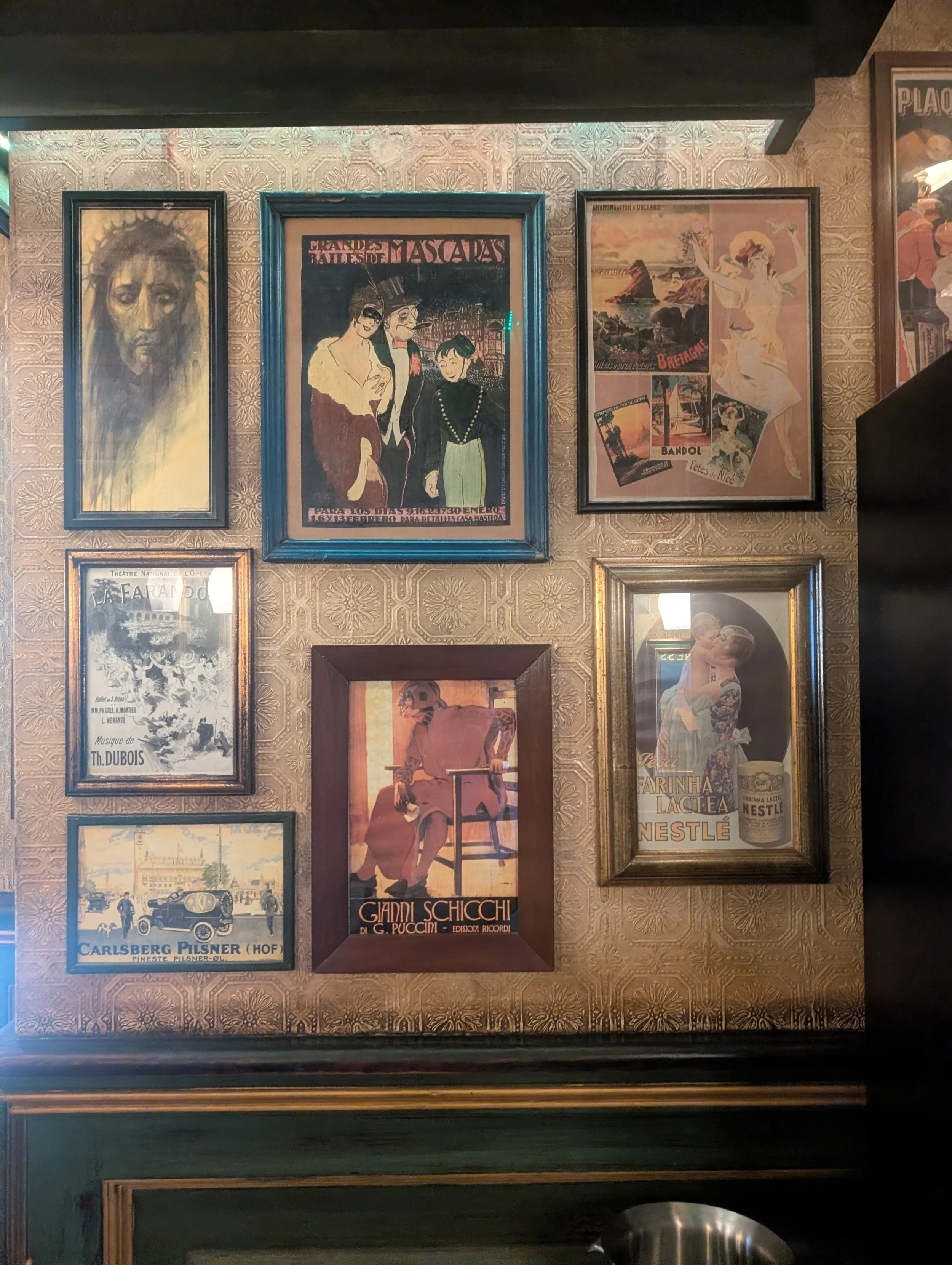 Wall decorated with vintage posters and artwork, including a portrait of Jesus Christ, a poster for a ballet, and various other vintage advertisements.