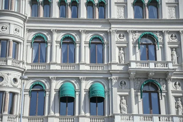 Close-up view of the ornate facade of a historic building with arched windows, decorative statues, and green awnings.