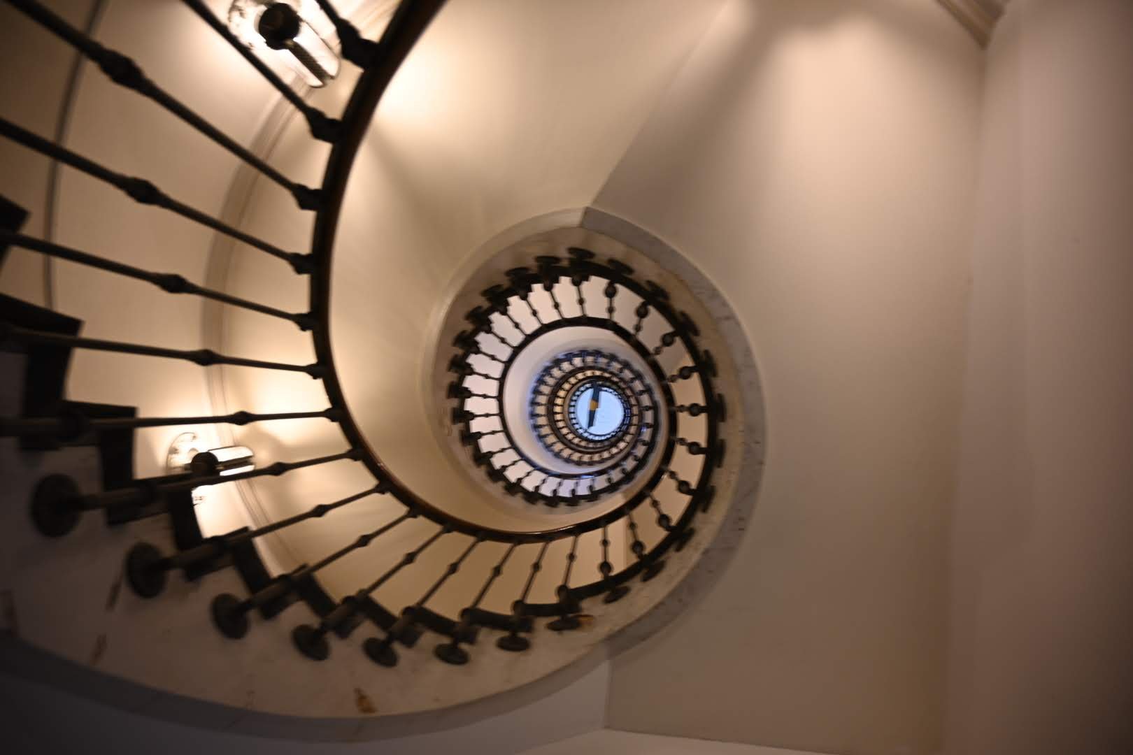 Spiral staircase viewed from top, with ornate black metal railing and a small clock at the center.