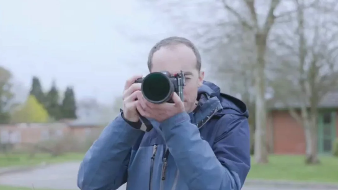 Tom is outdoors holding a Nikon Z8 camera and taking a photo.