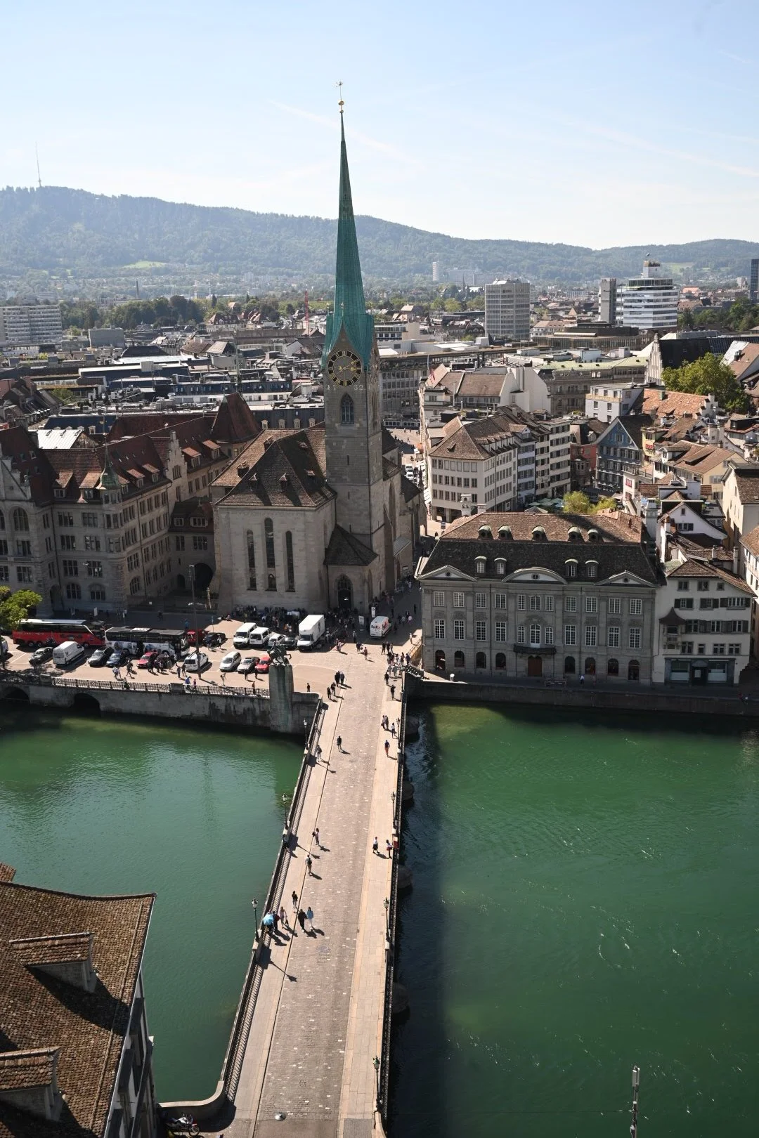 Aerial view of a historic city with a river running through it, a stone bridge, and a tall church with a green spire.