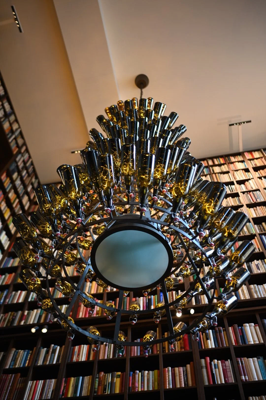Elegant chandelier with gold and black elements hanging in front of a large wall of books in a library.