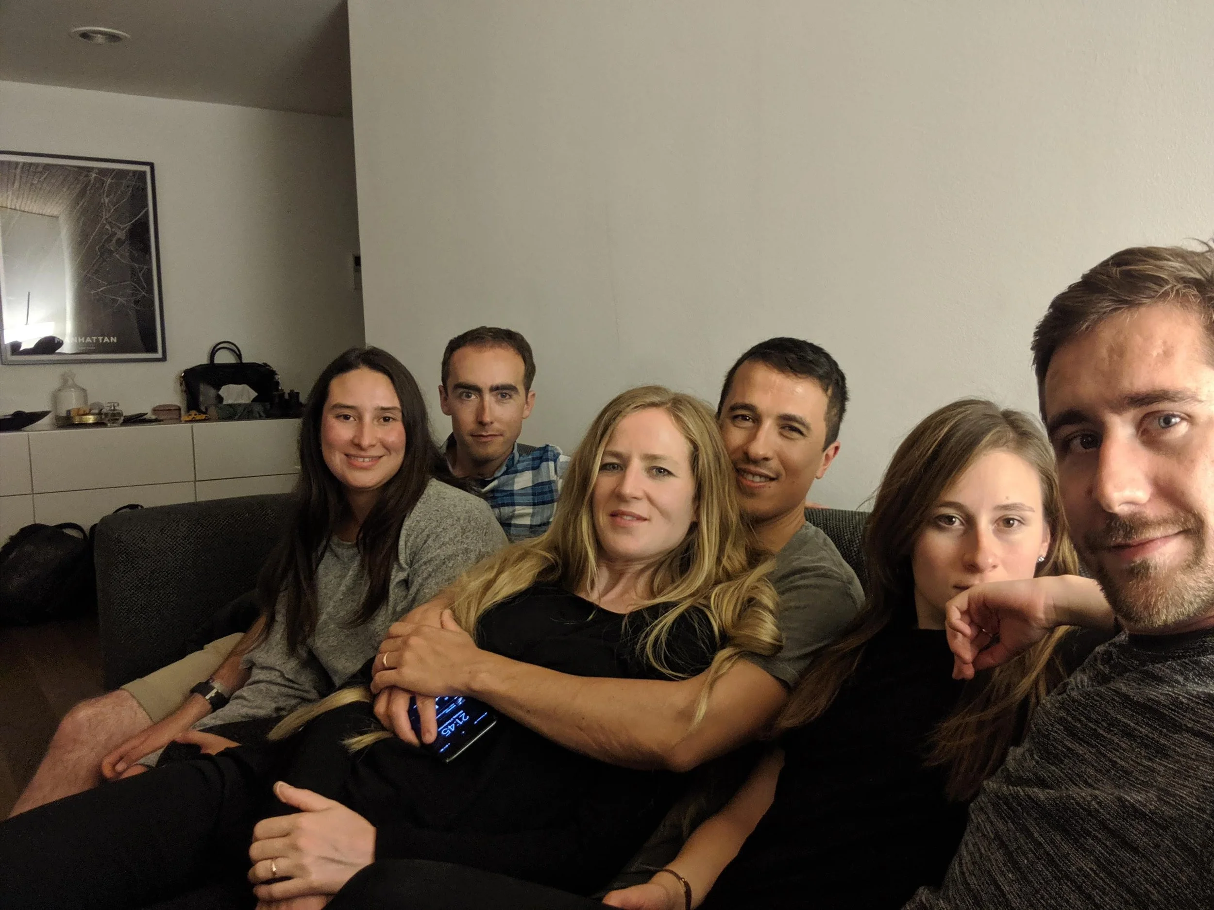 A group of people sitting on a couch, closely gathered together, smiling and enjoying each other's company in a cozy indoor setting.