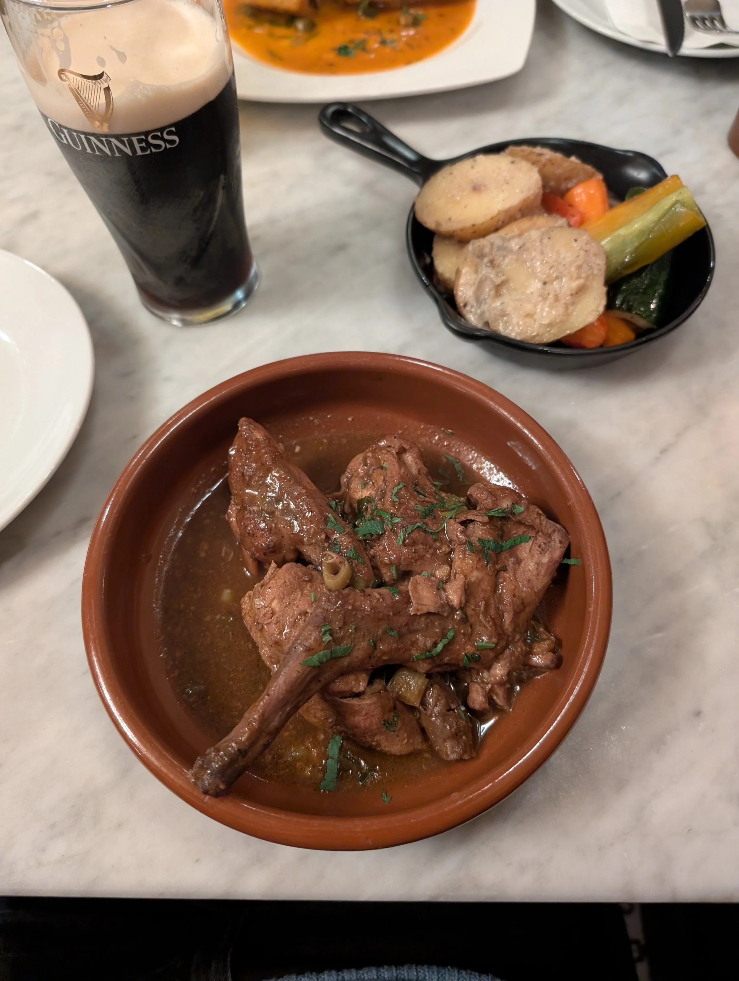 A plate of Irish stew with a smoked eel, a glass of Guinness beer, and a vegetable medley.