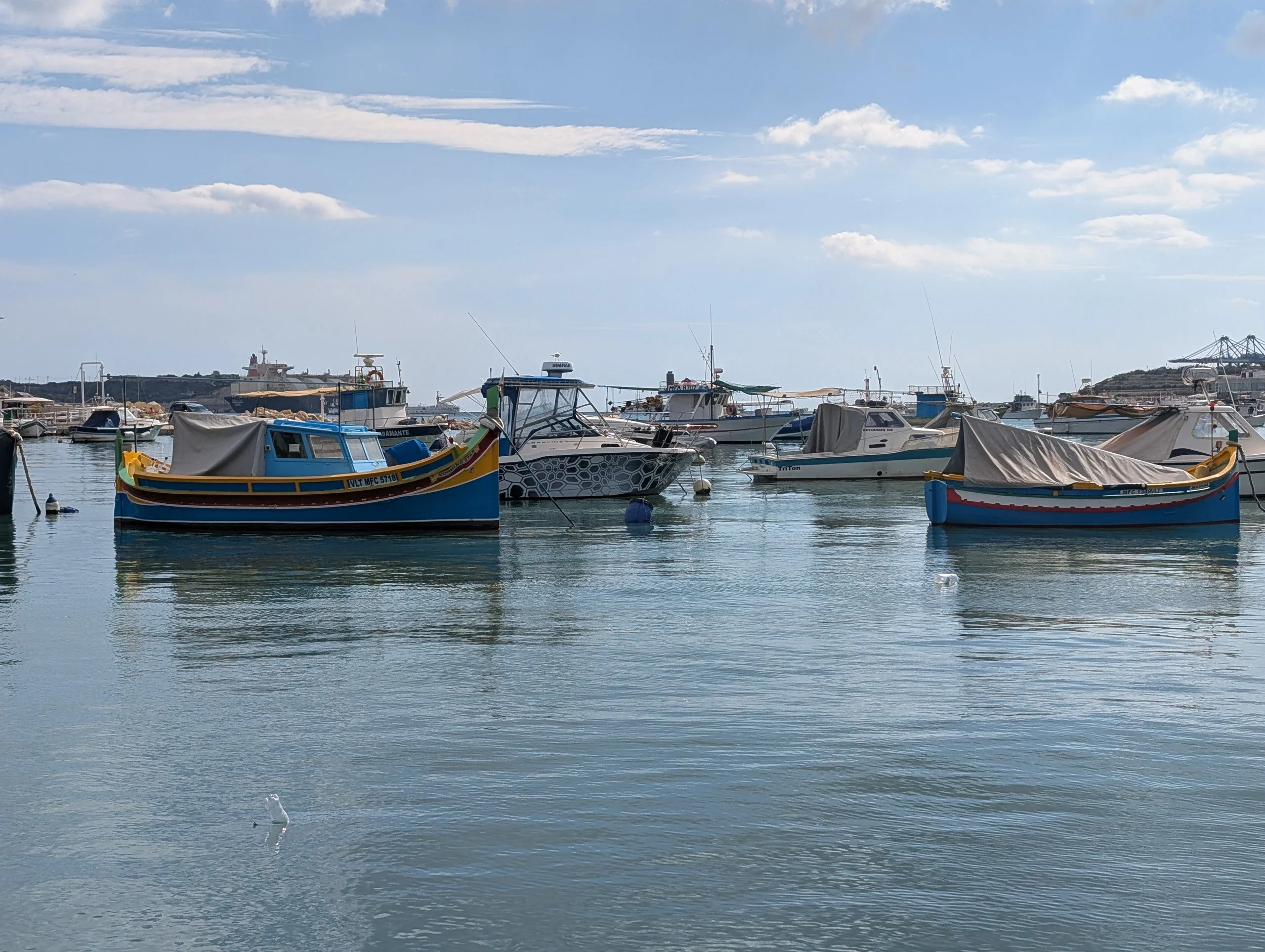 A harbor with multiple boats docked on calm water under a partly cloudy sky.