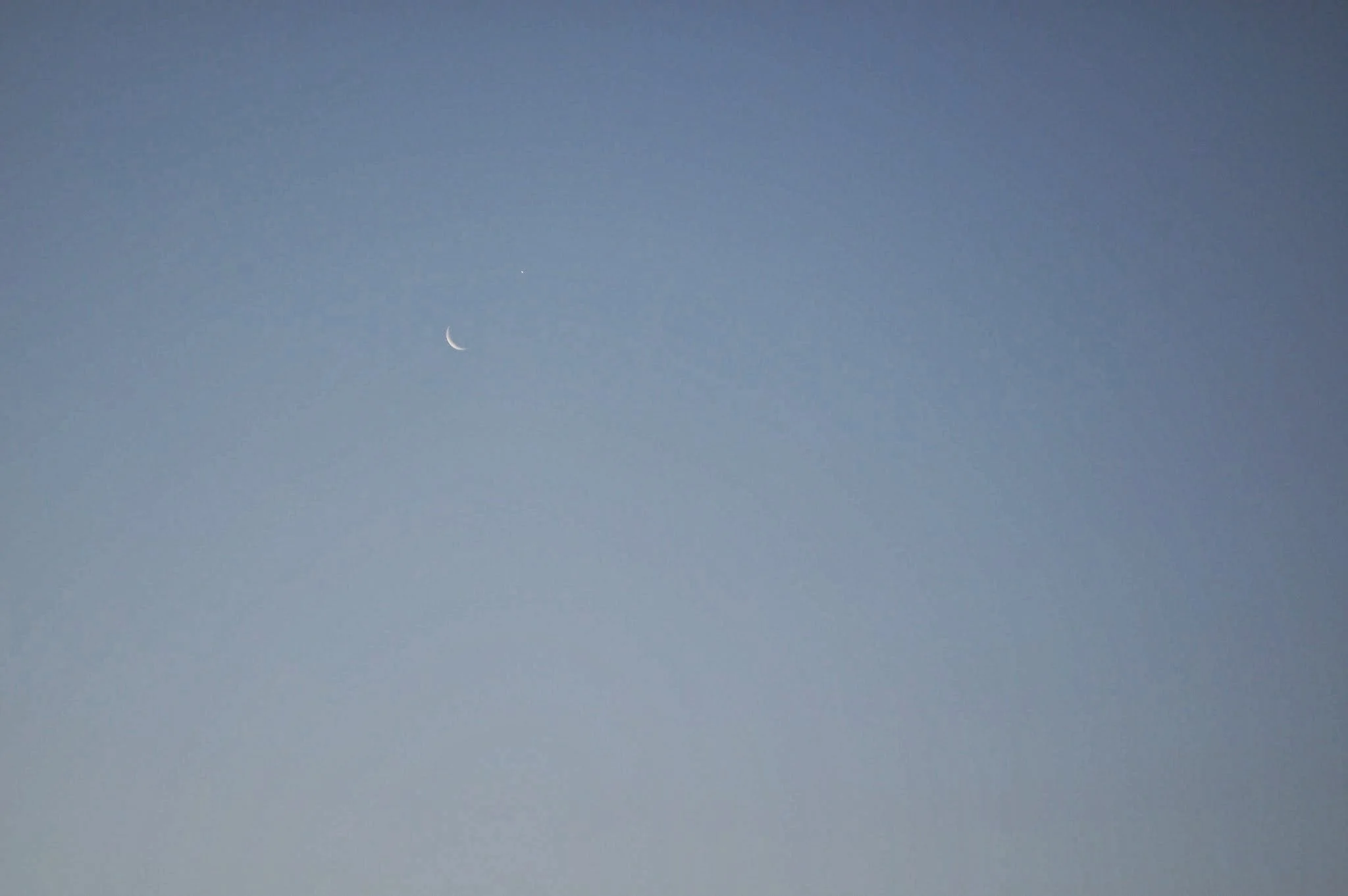 A clear sky featuring a crescent moon and a bright star or planet.