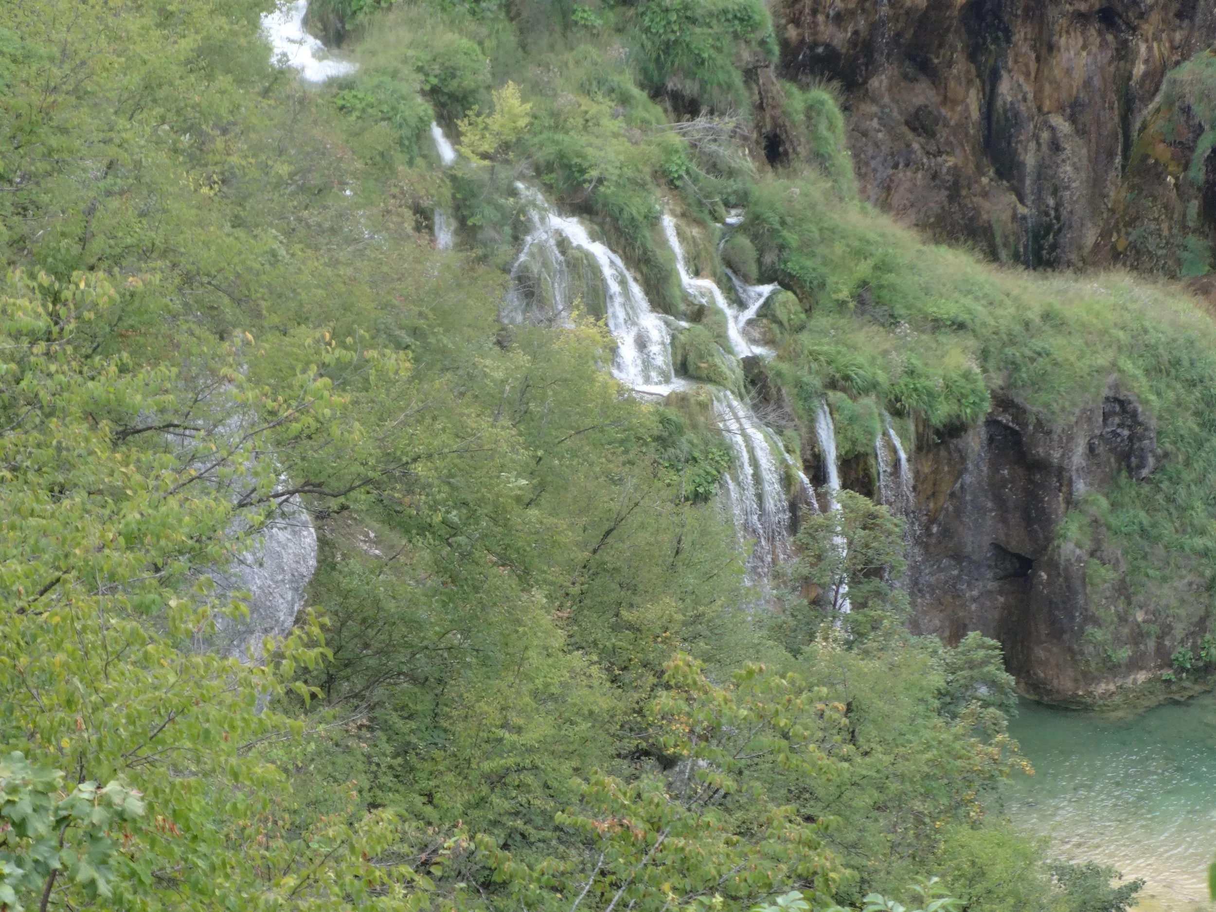 A waterfall flowing down a rocky, green hillside surrounded by lush trees and vegetation.