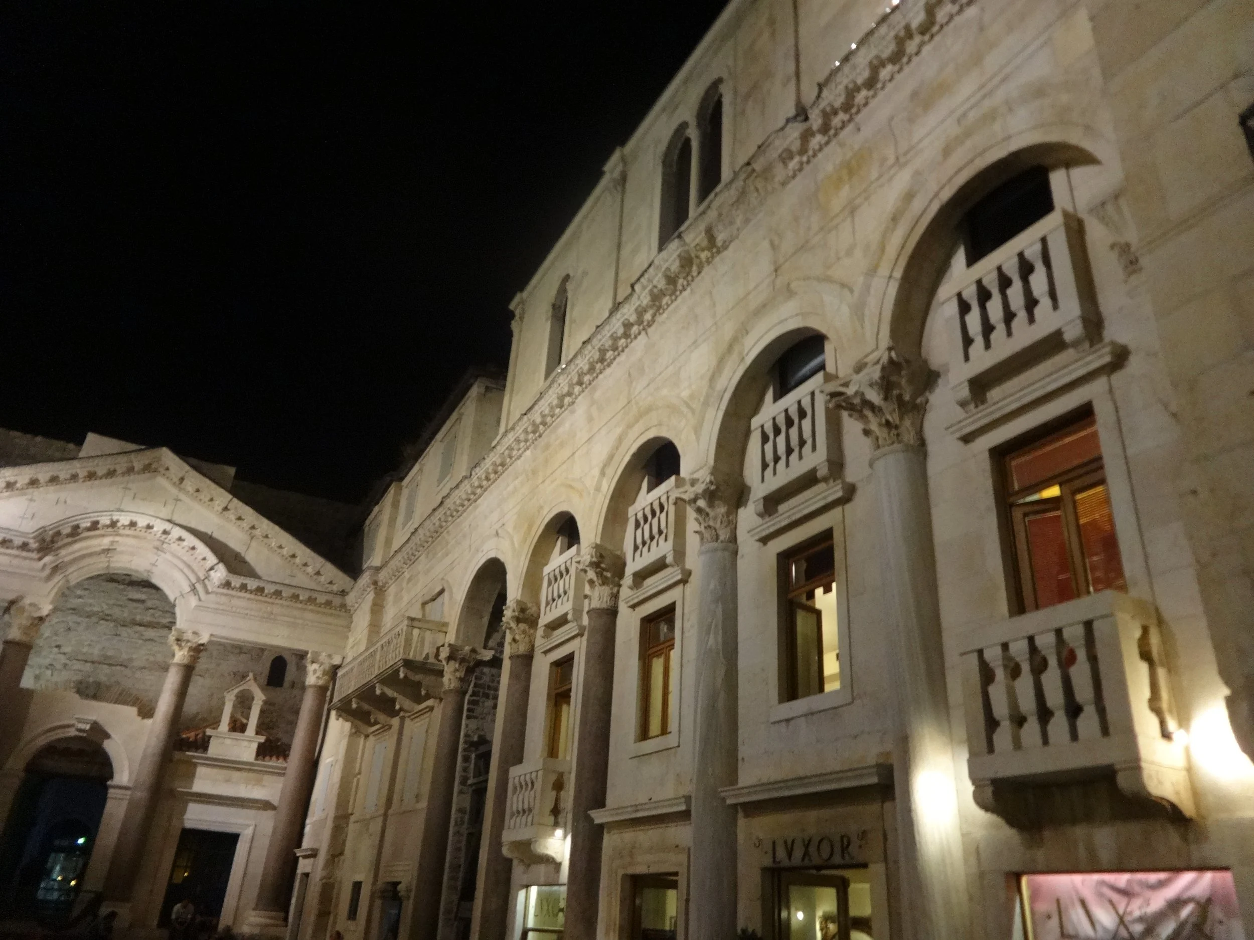 A historic building with classical architecture features, including columns, arches, and decorative stonework, illuminated at night.