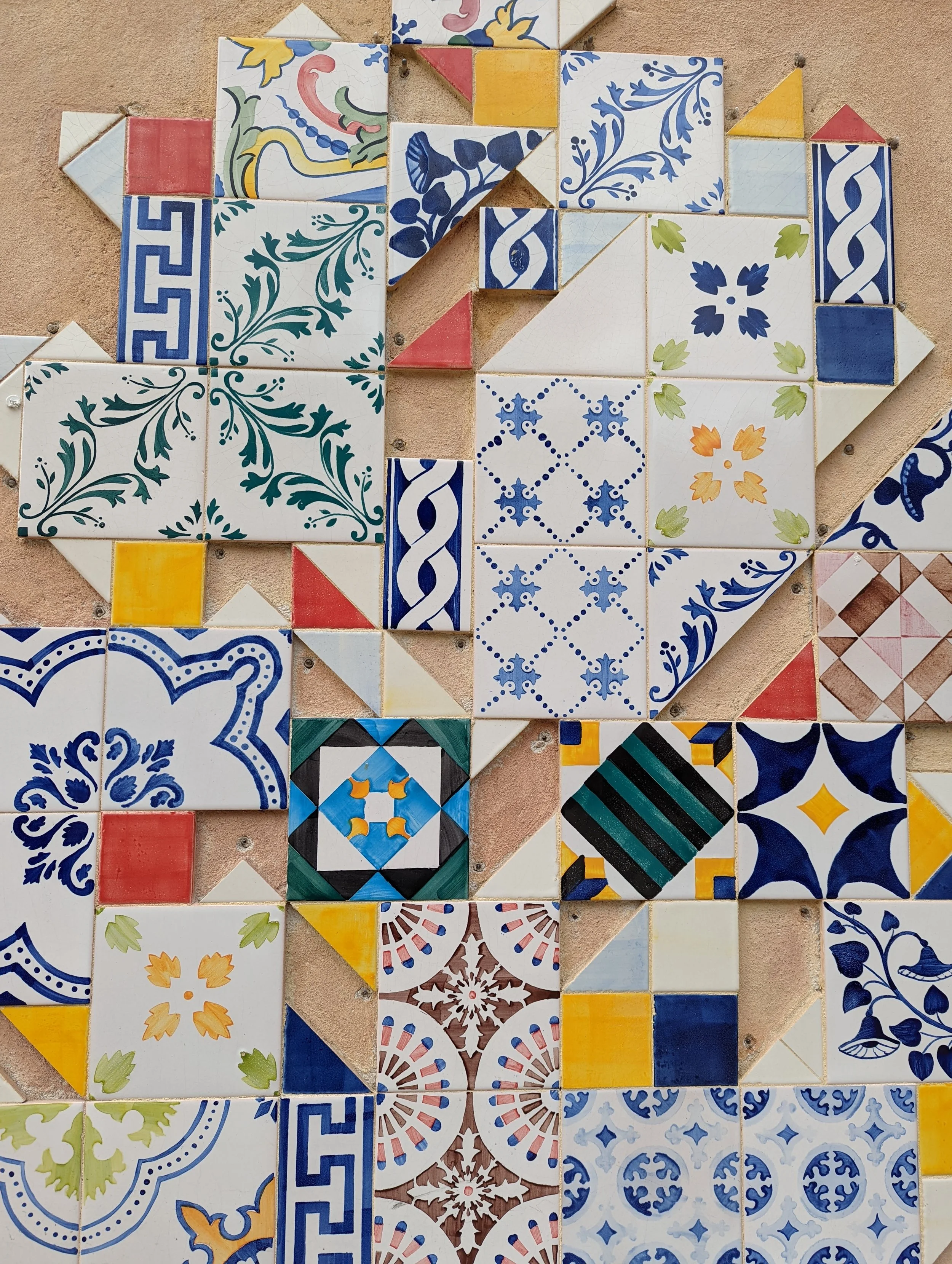Decorative ceramic tiles arranged in a pattern on a wall, featuring various traditional geometric and floral motifs in blue, yellow, red, green, and brown colors.