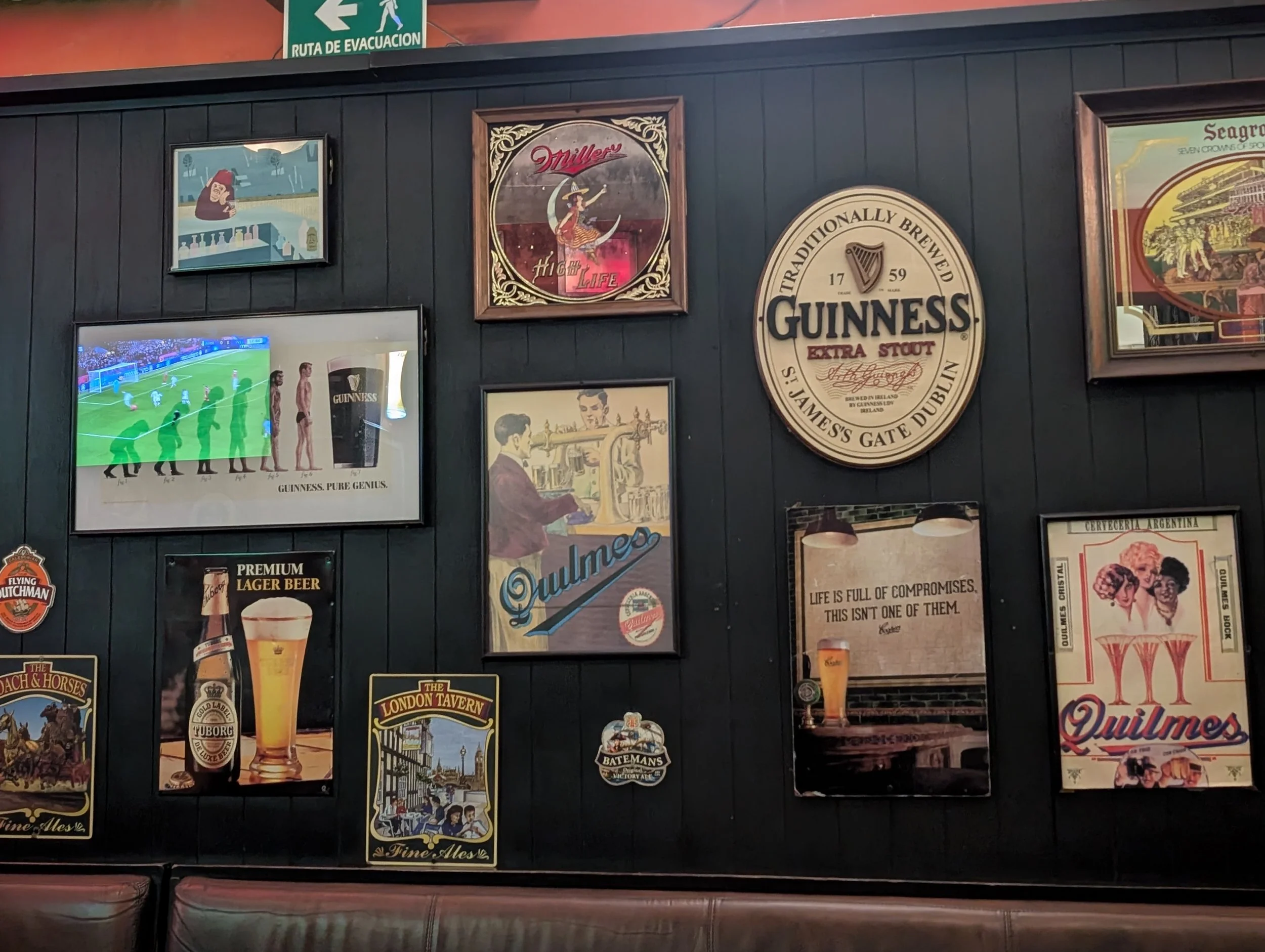 Wall decorated with vintage posters of Guinness and other brands, including a Guinness harp logo, a soccer match TV broadcast, and a sign for an emergency evacuation route.