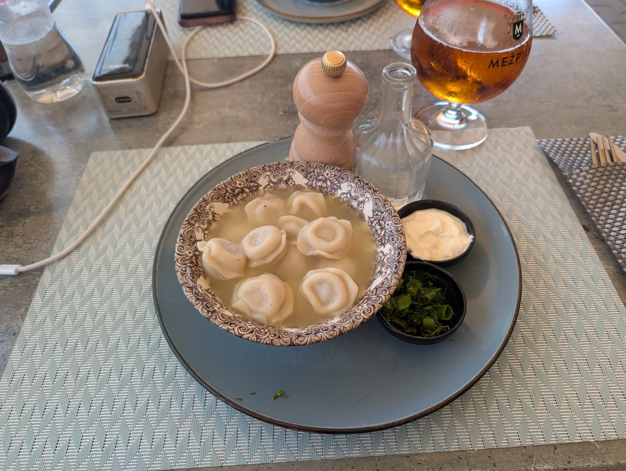 Dumplings in broth with side dishes, a glass of beer, and table setting.