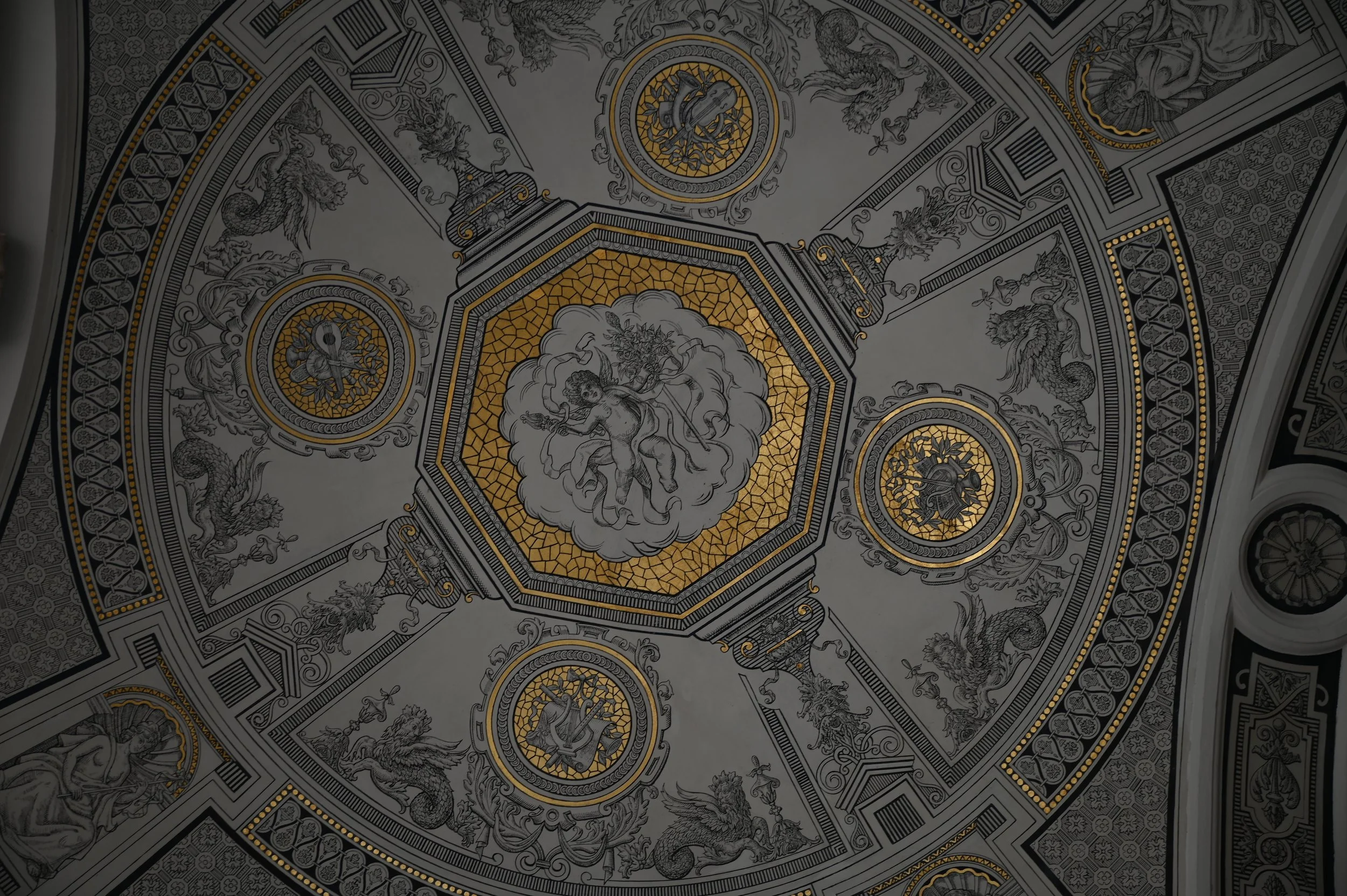 Decorative ceiling with detailed artwork and gold accents, featuring mythical creatures and intricate patterns.