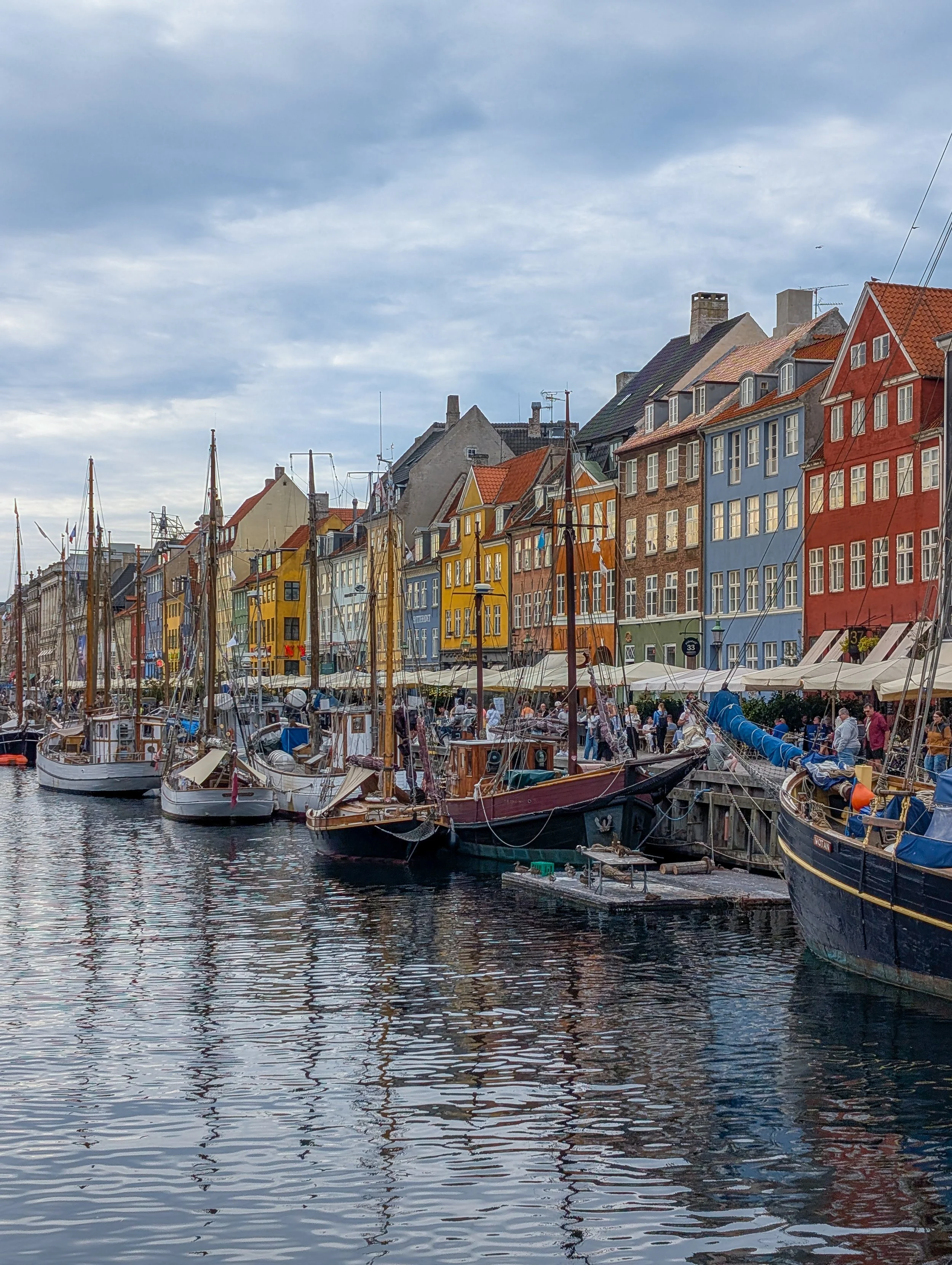 Colorful buildings with boats docked on a river, cloudy sky overhead.