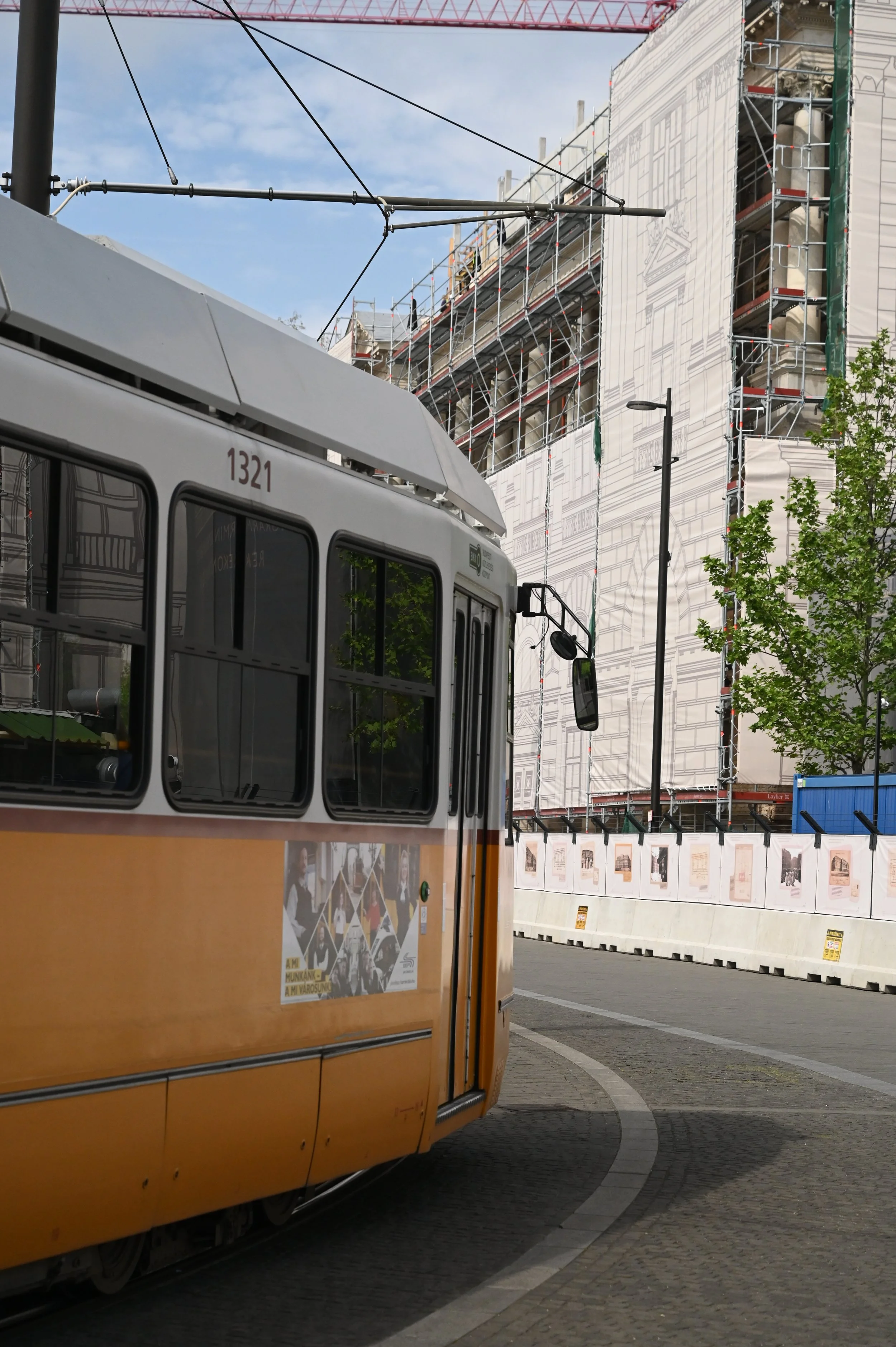 A yellow tram on a curved cobblestone street with a construction site in the background, scaffolding surrounding a building and a white tarp.