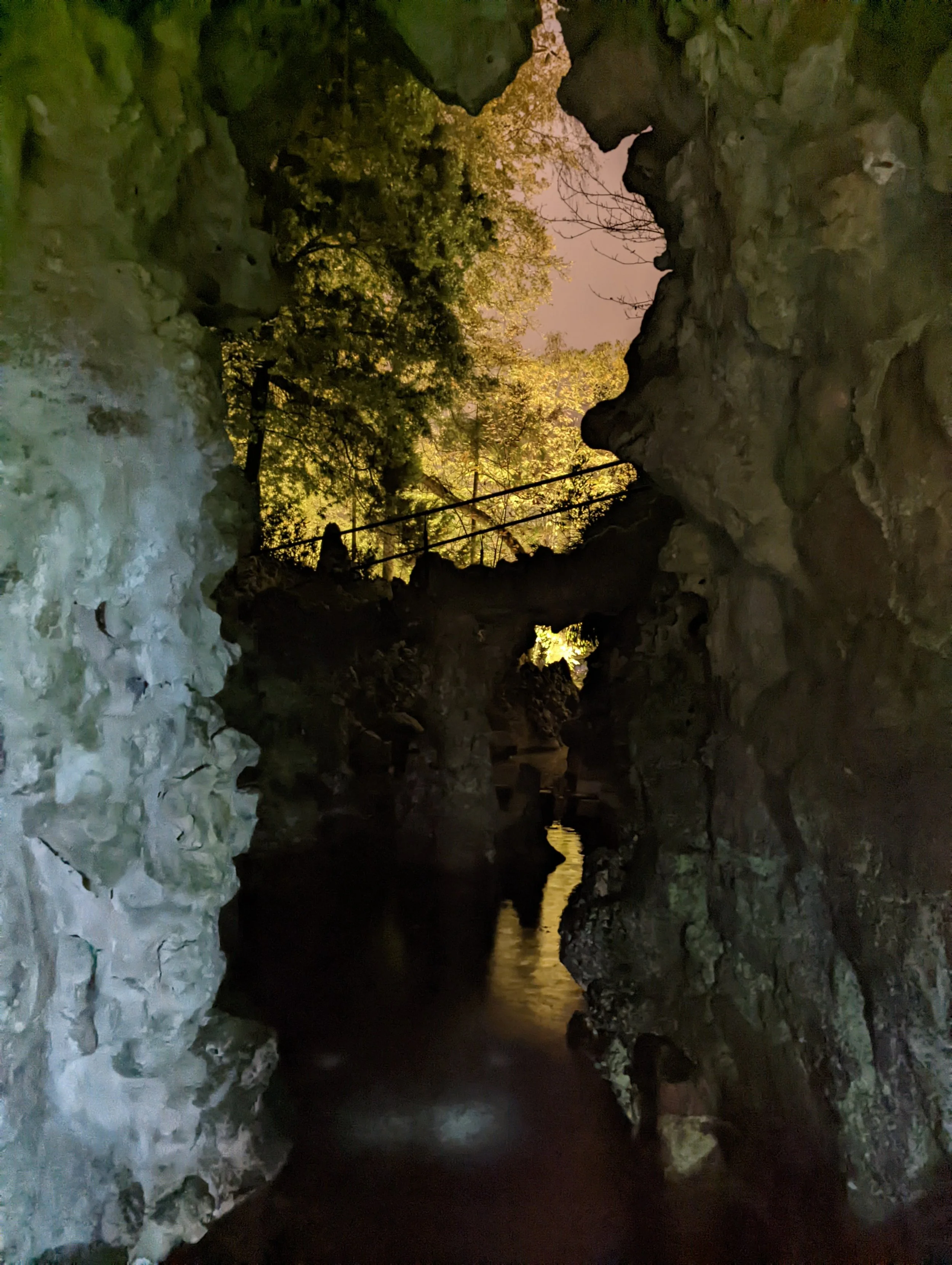 Nighttime view of a rocky canyon with a small stream or river running through it, illuminated by artificial lighting that highlights the rocky surfaces and trees in the background.
