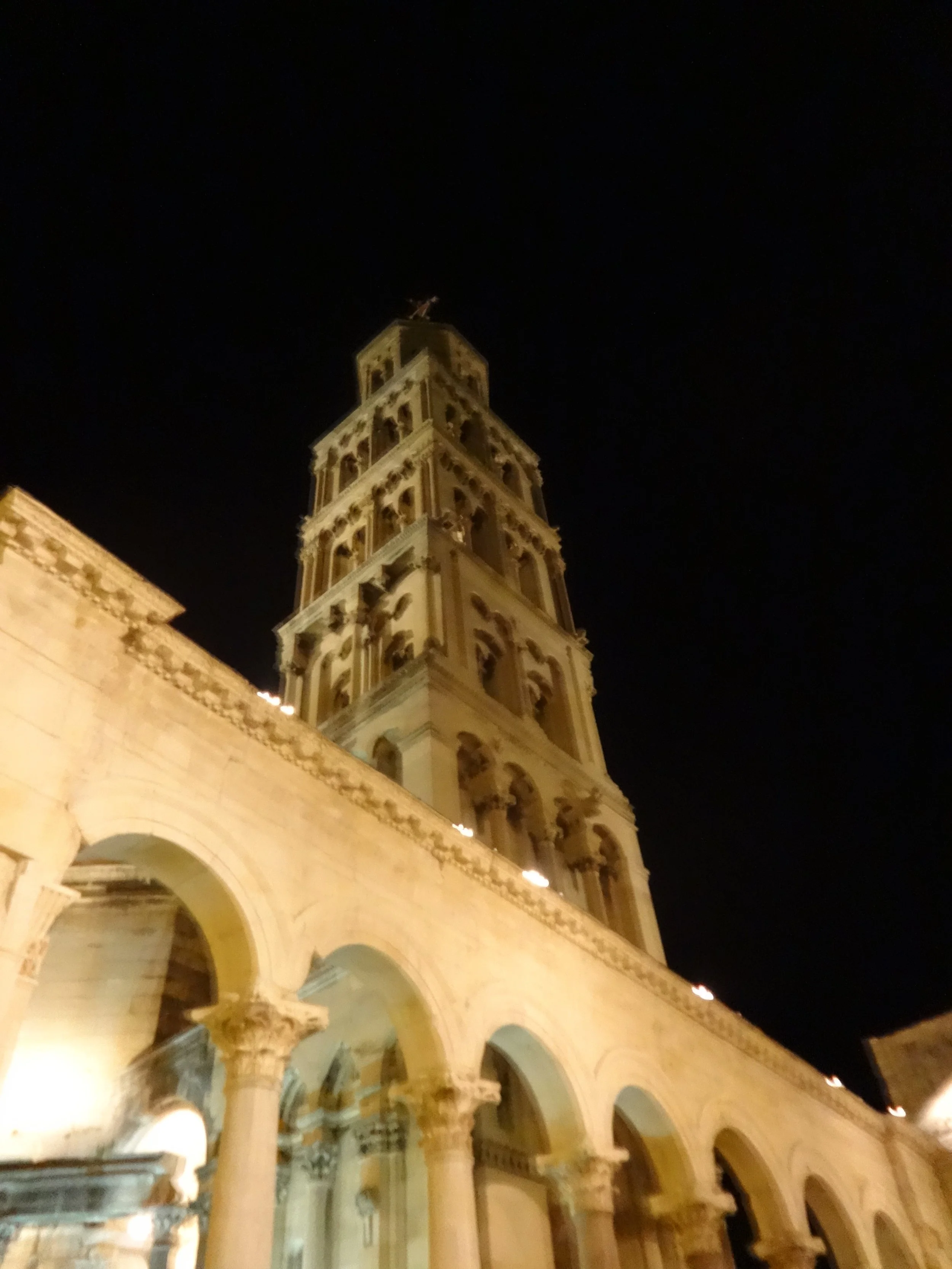 A tall, ornate clock tower illuminated at night, part of a historic building with arches and columns.
