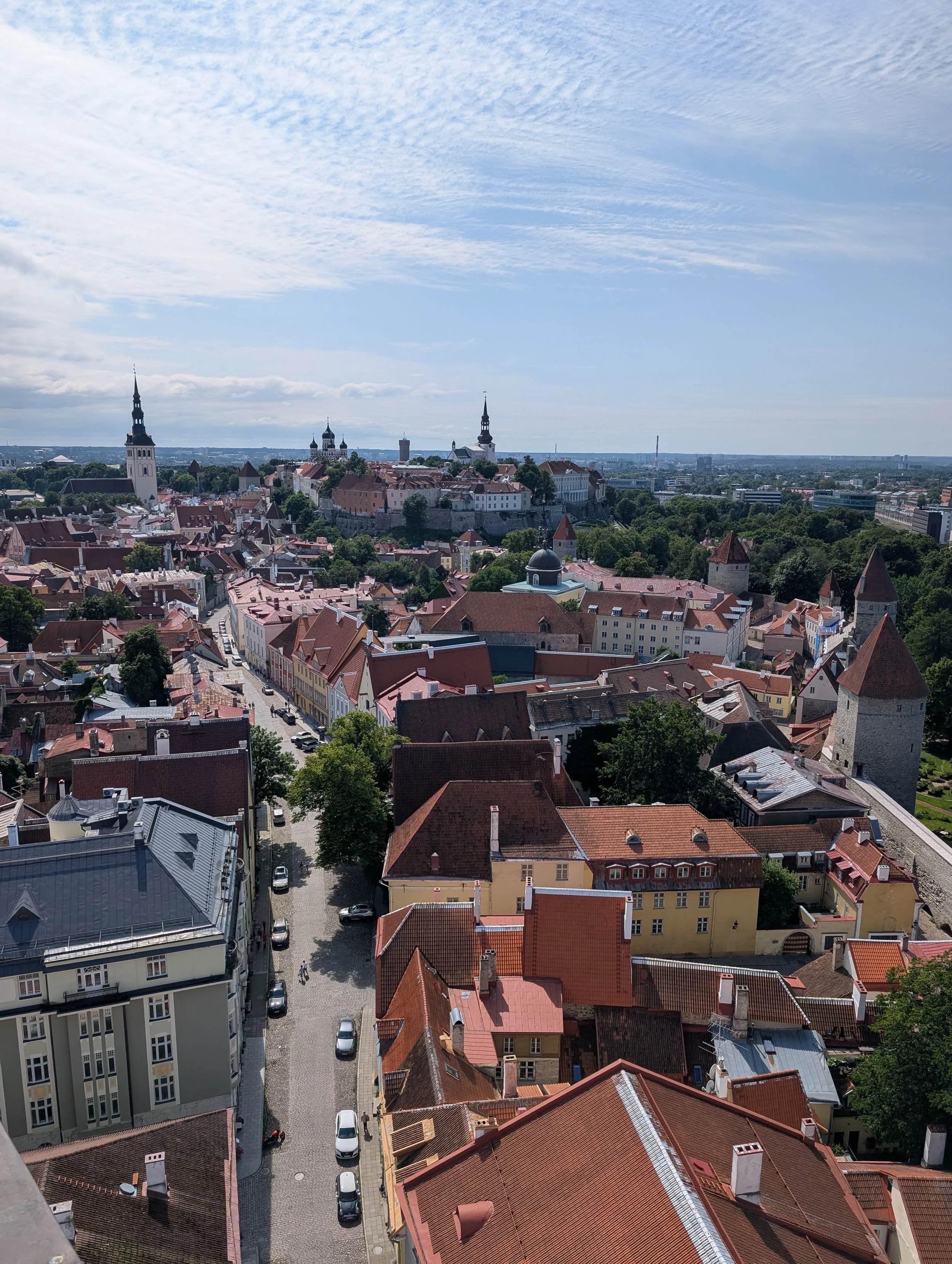 A cityscape view with historic buildings, church steeples, and a mix of old and modern architecture under a partly cloudy sky, taken from an elevated perspective.