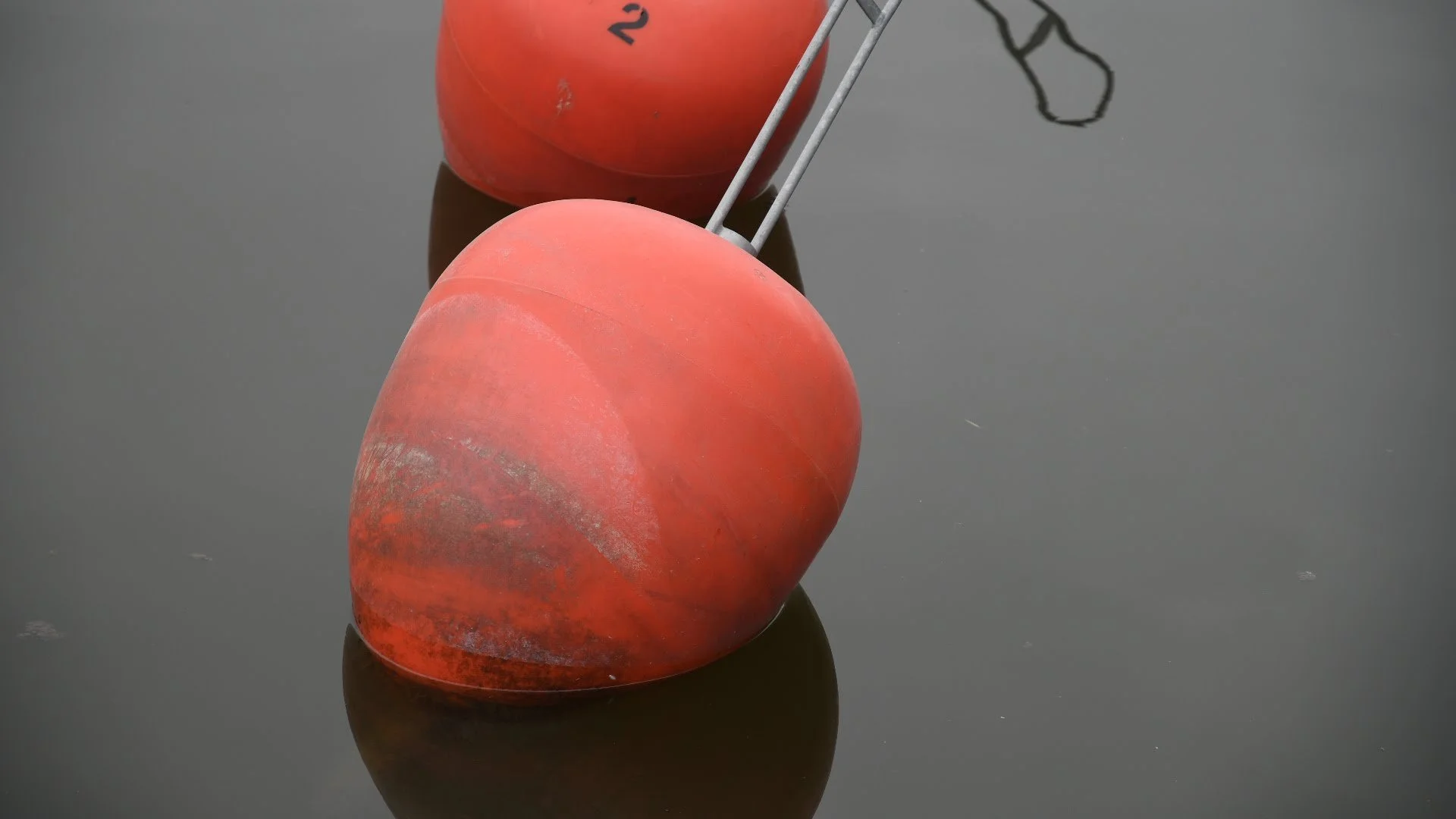Two red and orange buoys floating on dark water, with reflections visible on the surface.