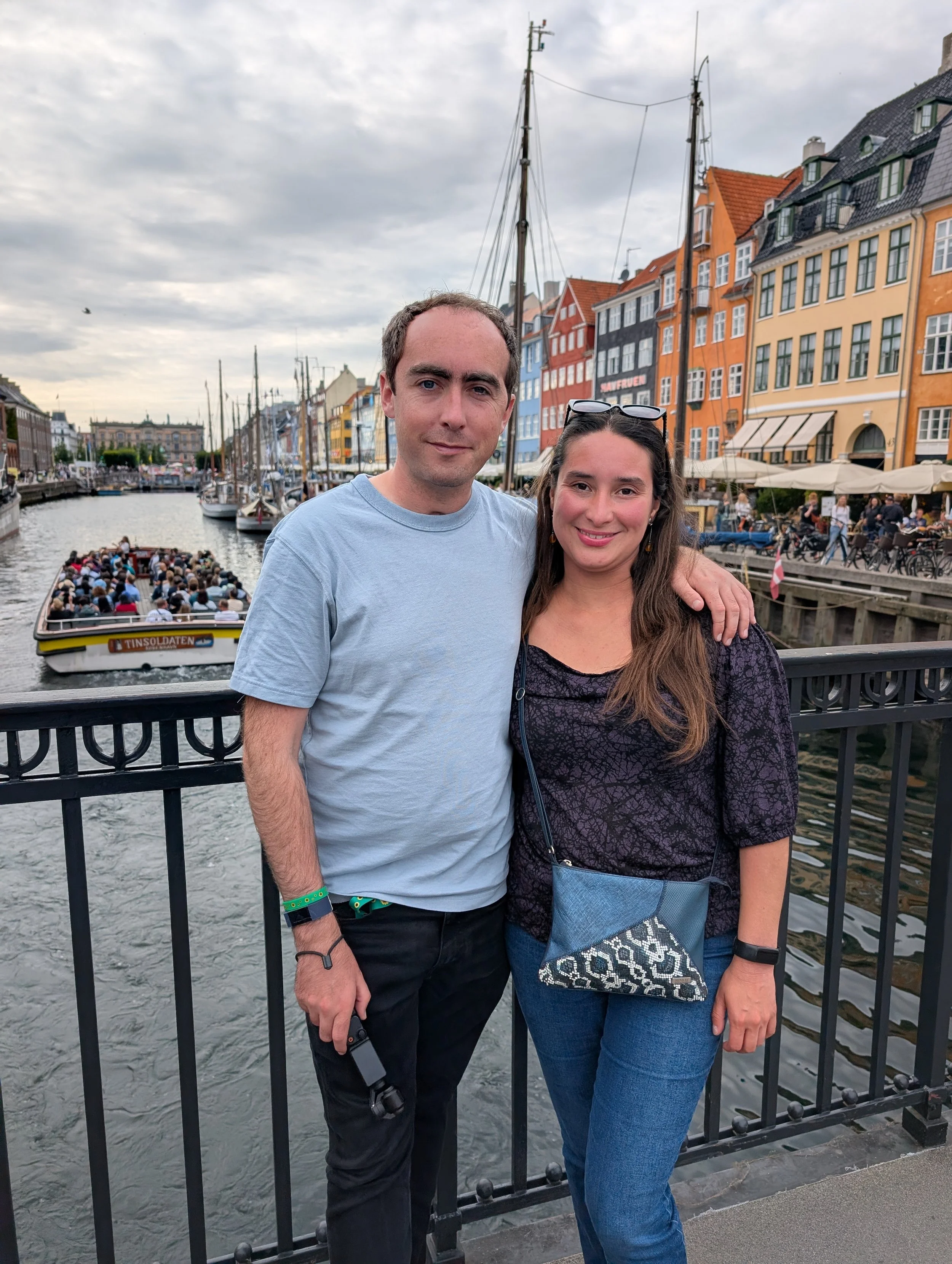 A man and woman posing together on a bridge over a canal with colorful buildings and boats in the background.