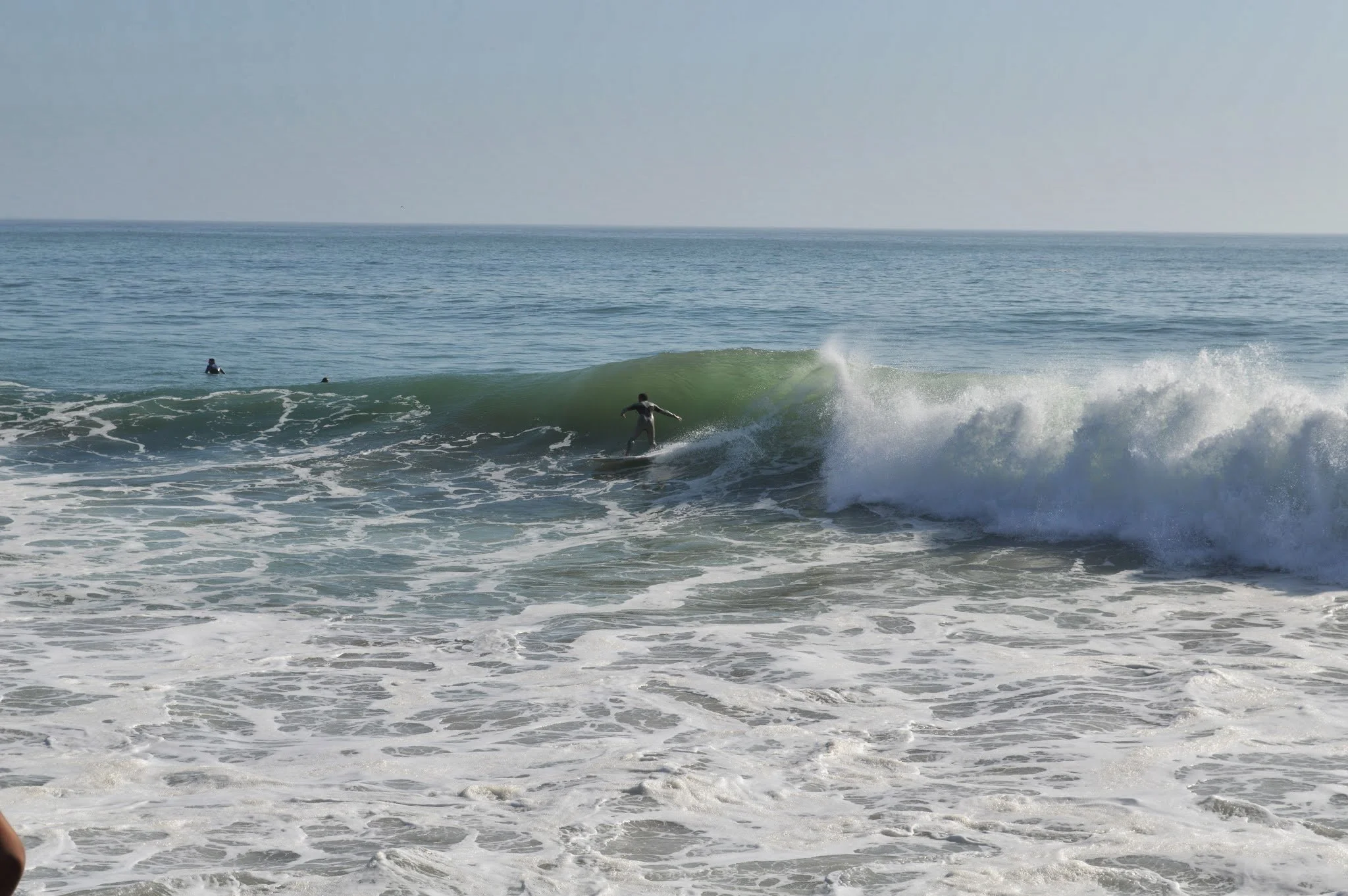 A person surfing on a wave in the ocean with a clear sky in the background.