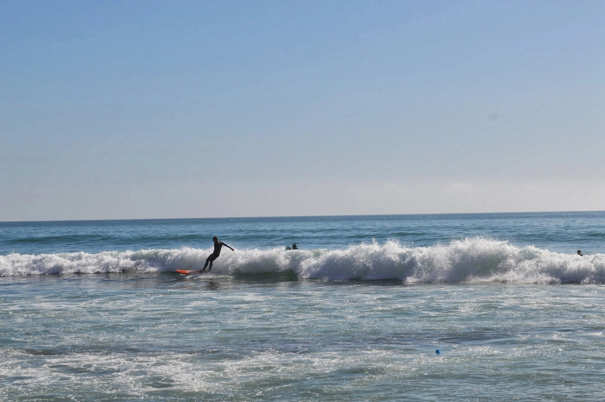 People surfing and swimming in the ocean near the shoreline on a sunny day.