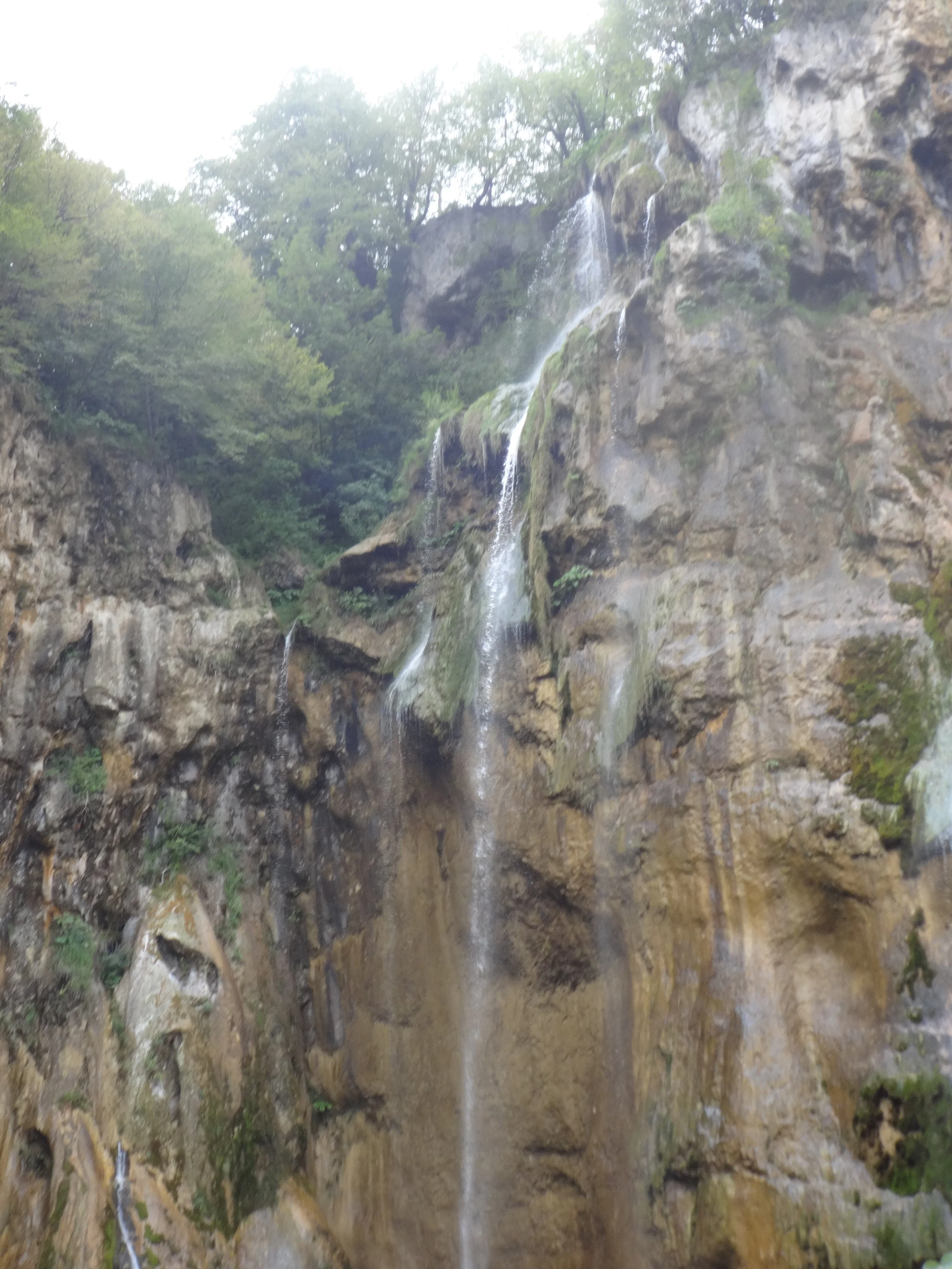 A small waterfall cascading down a rocky cliff surrounded by green trees.